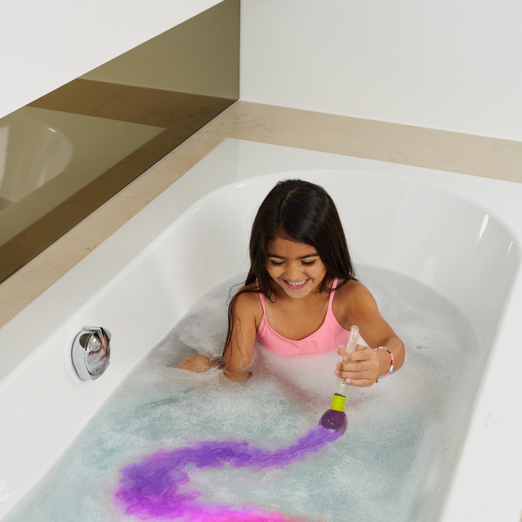Girl painting pink and purple trails in the bath water with the bath bomb brush