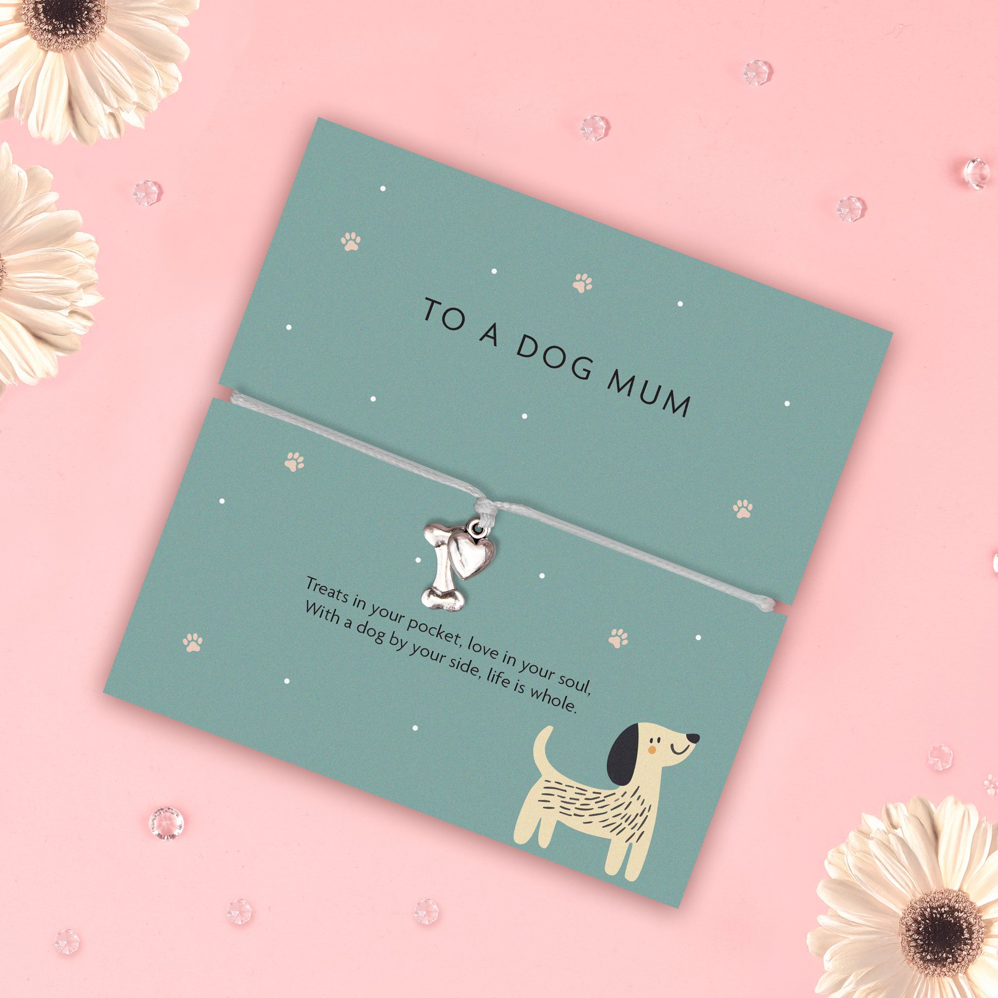 Karte «To a Dog Mum» mit grauem Armband schräg auf Rosa zwischen weissen Gerbera-Blüten