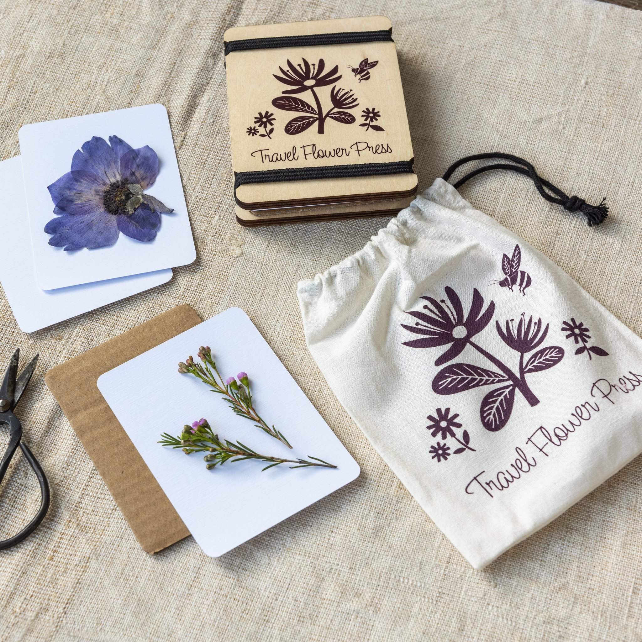 Pressa da viaggio con fiore blu pressato e sacchetto su lino