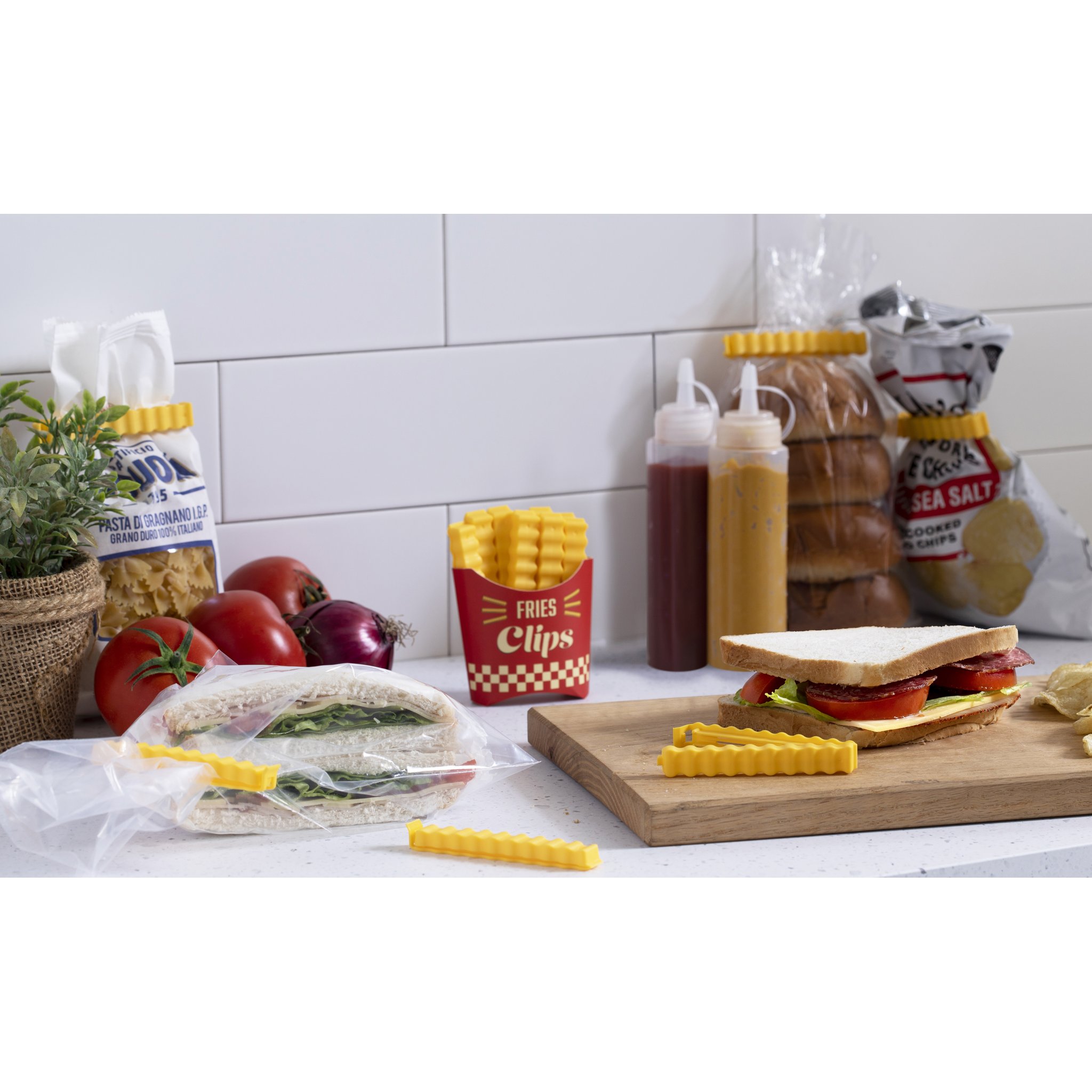 Pommes Tütenklammern-Box neben Pasta-Tüte, Saucenflaschen und Sandwich