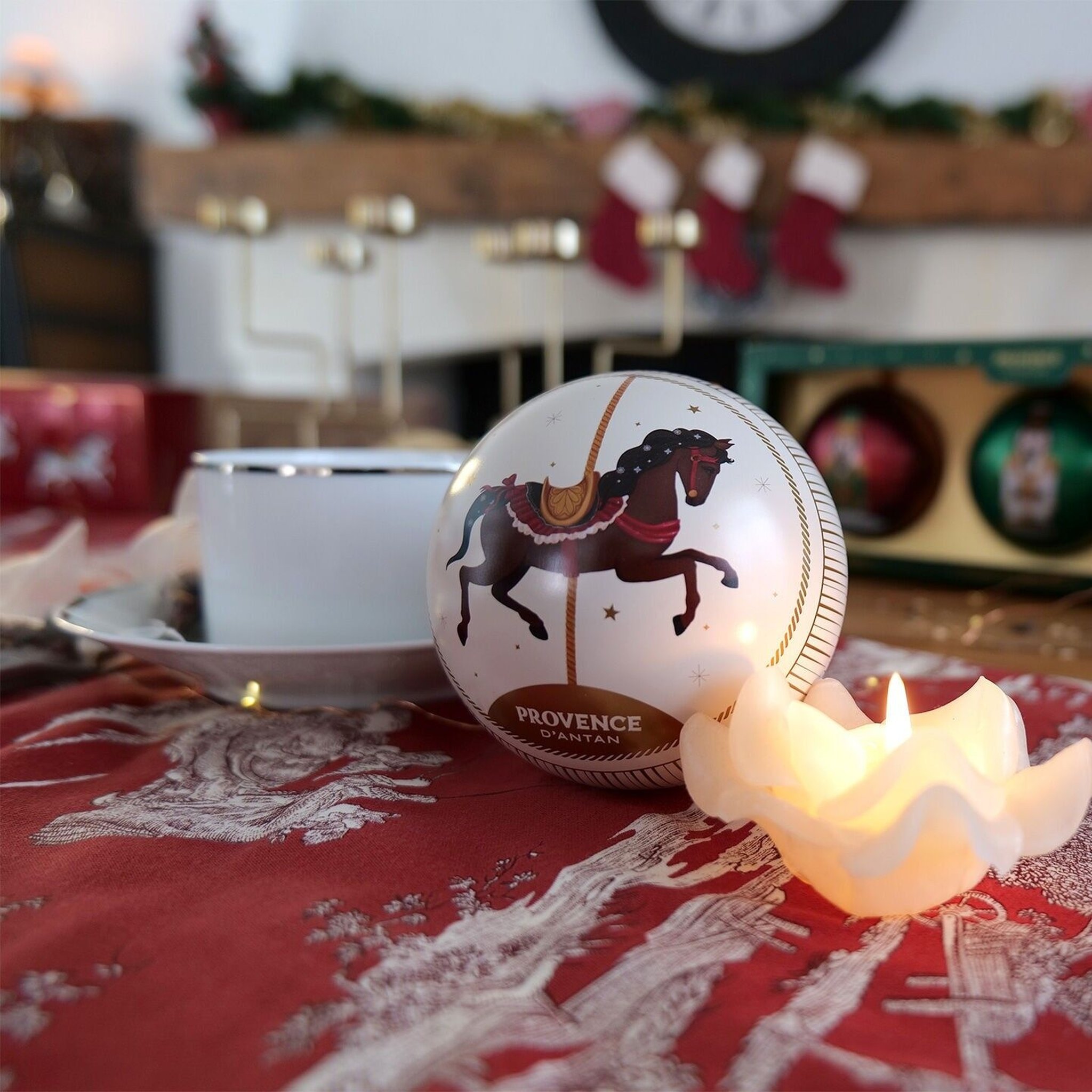 Perlweisse Kugel aus dem Set neben Teetasse und brennender Kerze auf rotem Tischläufer