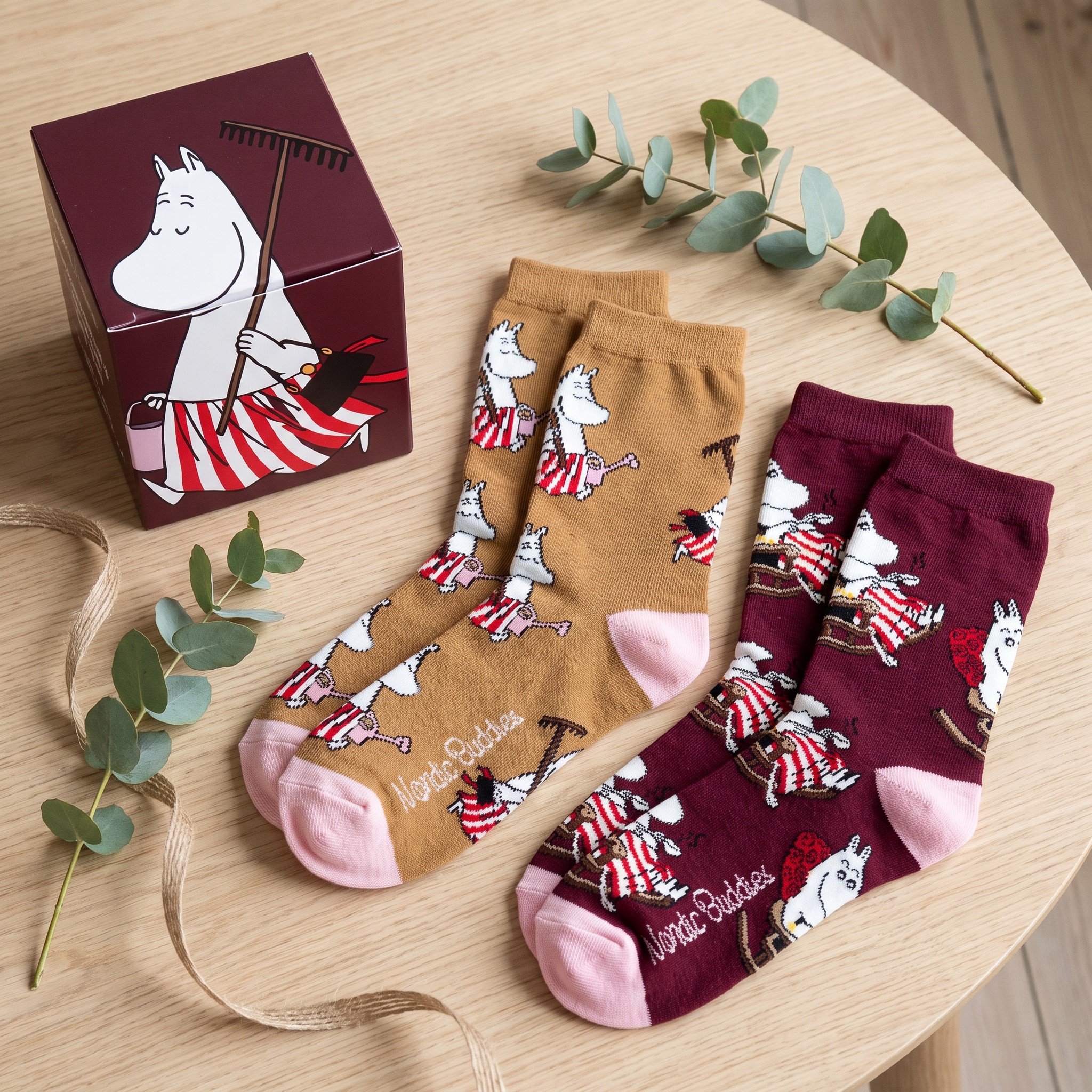 Le due paia di calze Moomin accanto alla scatola regalo rosso scuro su un tavolo di legno