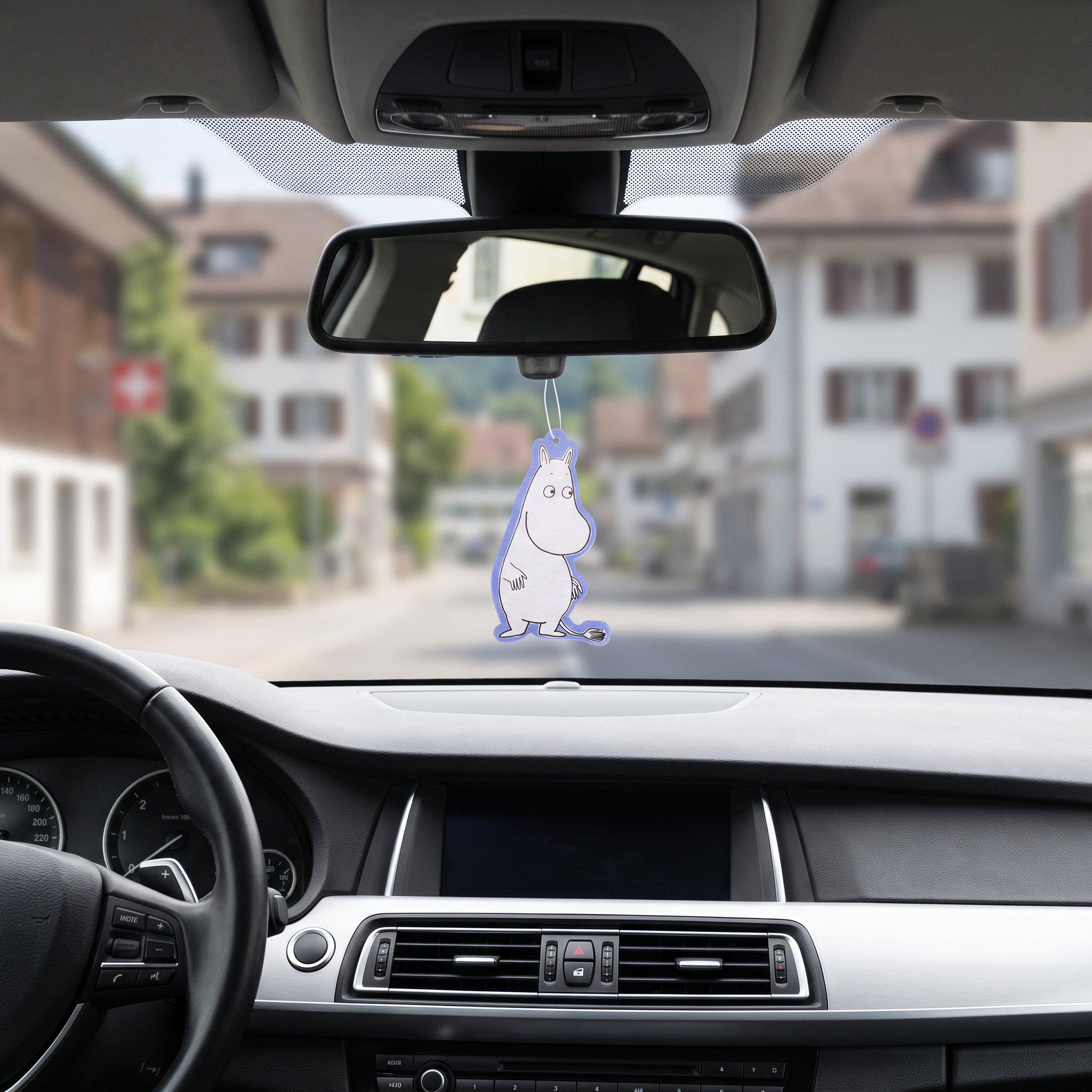 Car interior with the Moomin air freshener on the rear-view mirror, village street outside