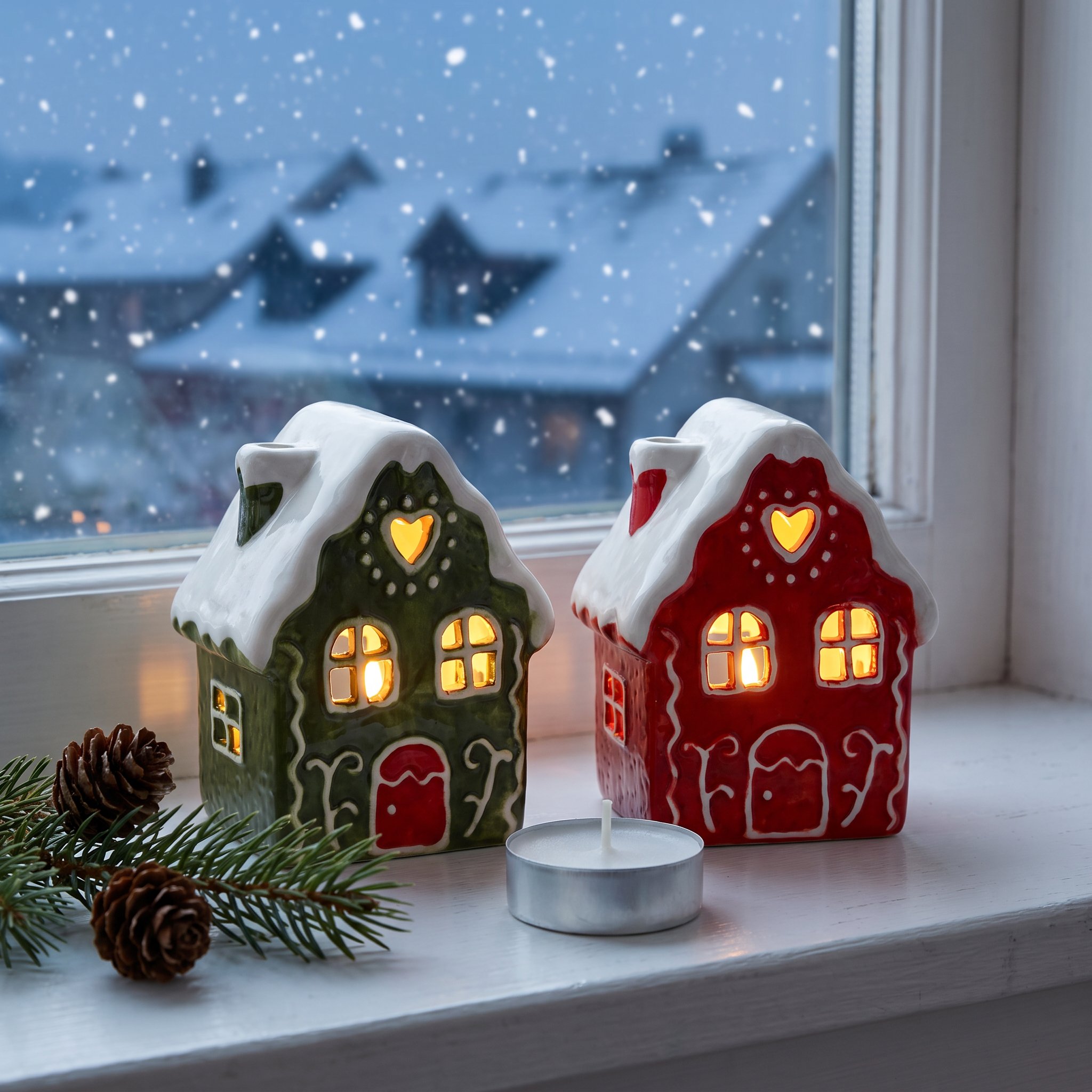Rotes und grünes Lebkuchenhaus mit brennendem Teelicht auf der Fensterbank, draussen fällt Schnee
