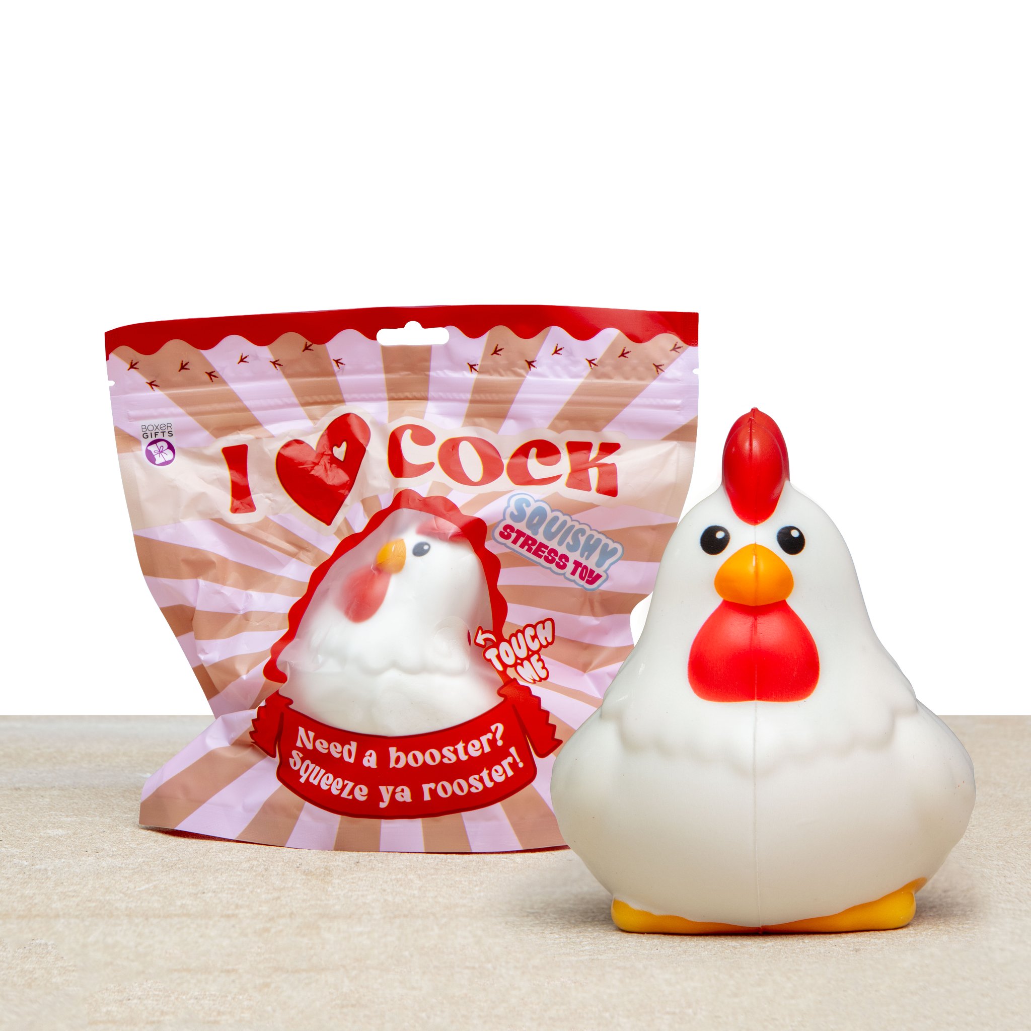 Squishy coq I Love Cock vu de face à côté de son sachet imprimé sur une table claire