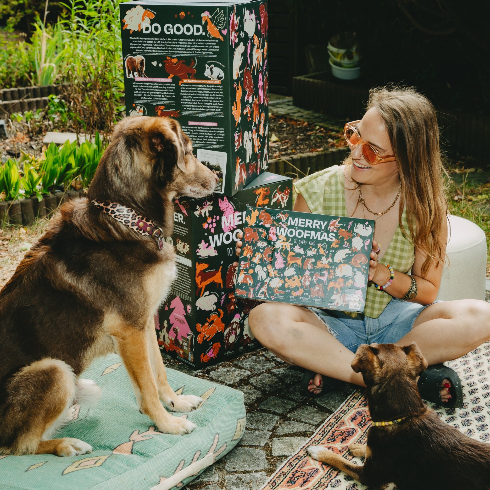 Calendrier de l'Avent pour chiens avec Winter Cookies – femme avec deux chiens montrant le calendrier «Merry Woofmas» au jardin
