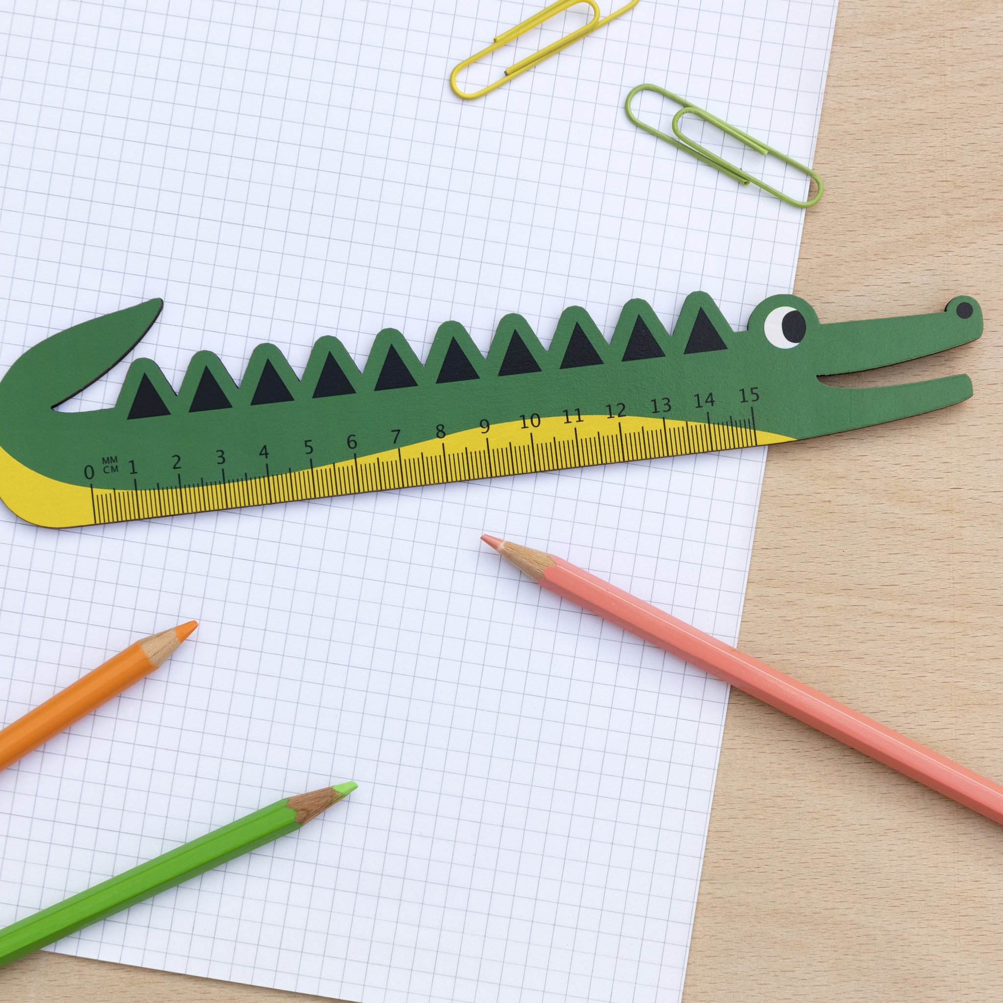 Wooden crocodile ruler on squared paper with paper clips and pencils