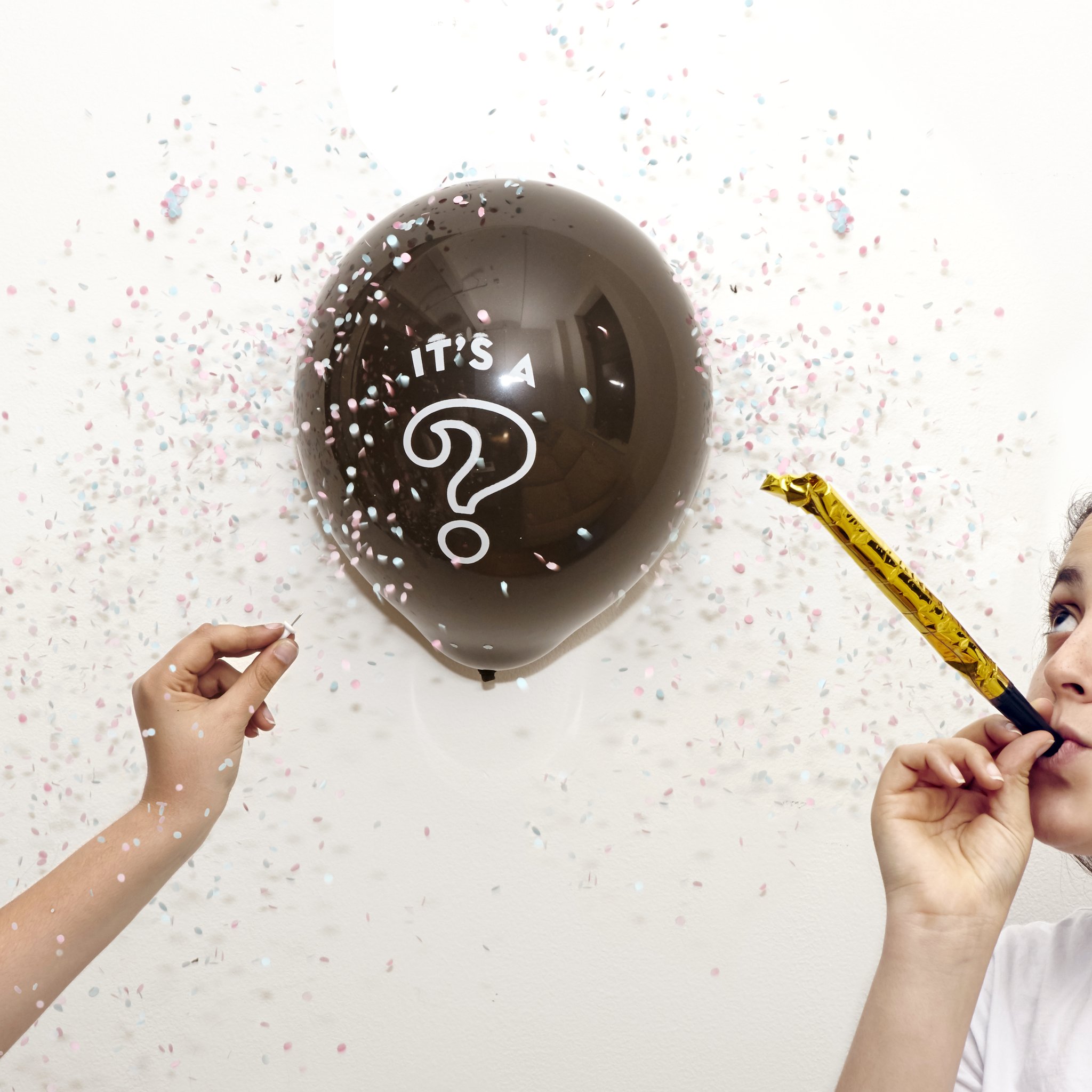 Ballon noir avec point d'interrogation et confettis, enfant soufflant dans la trompette