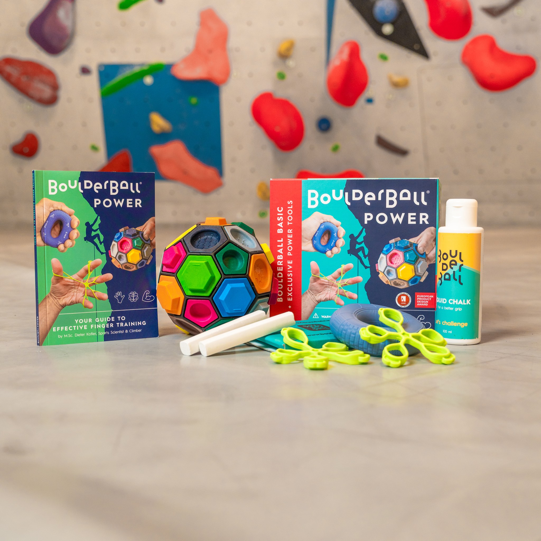 Set POWER con Boulderball, libretti e magnesite liquida davanti a una parete boulder in palestra