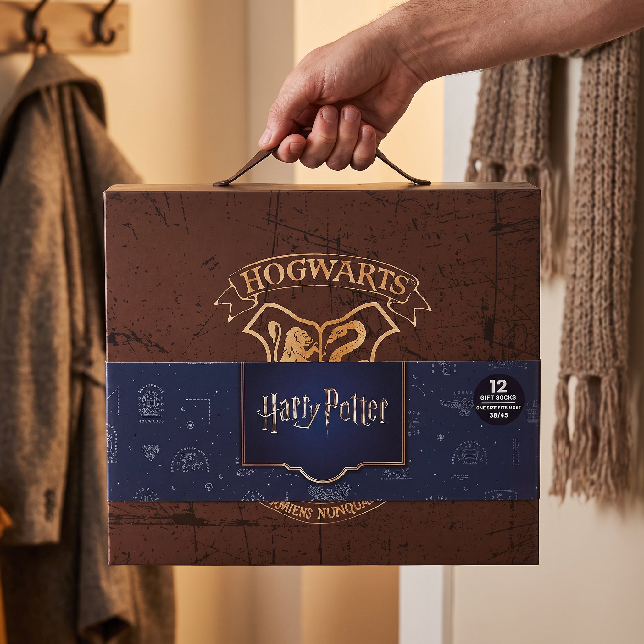 Hand carrying the Harry Potter sock gift box by its strap, cardboard box with Hogwarts crest and «12 Gift Socks» sleeve
