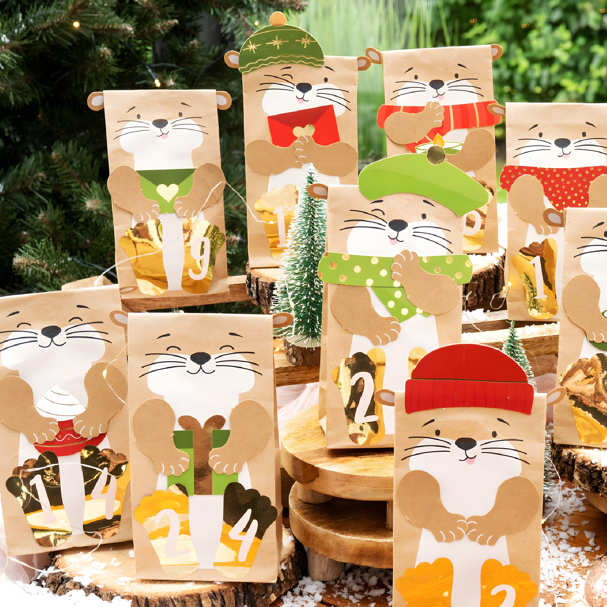 Otter-Tüten mit Mützen, Schals und goldenen Zahlen auf Holzscheiben vor Tannenbäumchen im Schnee