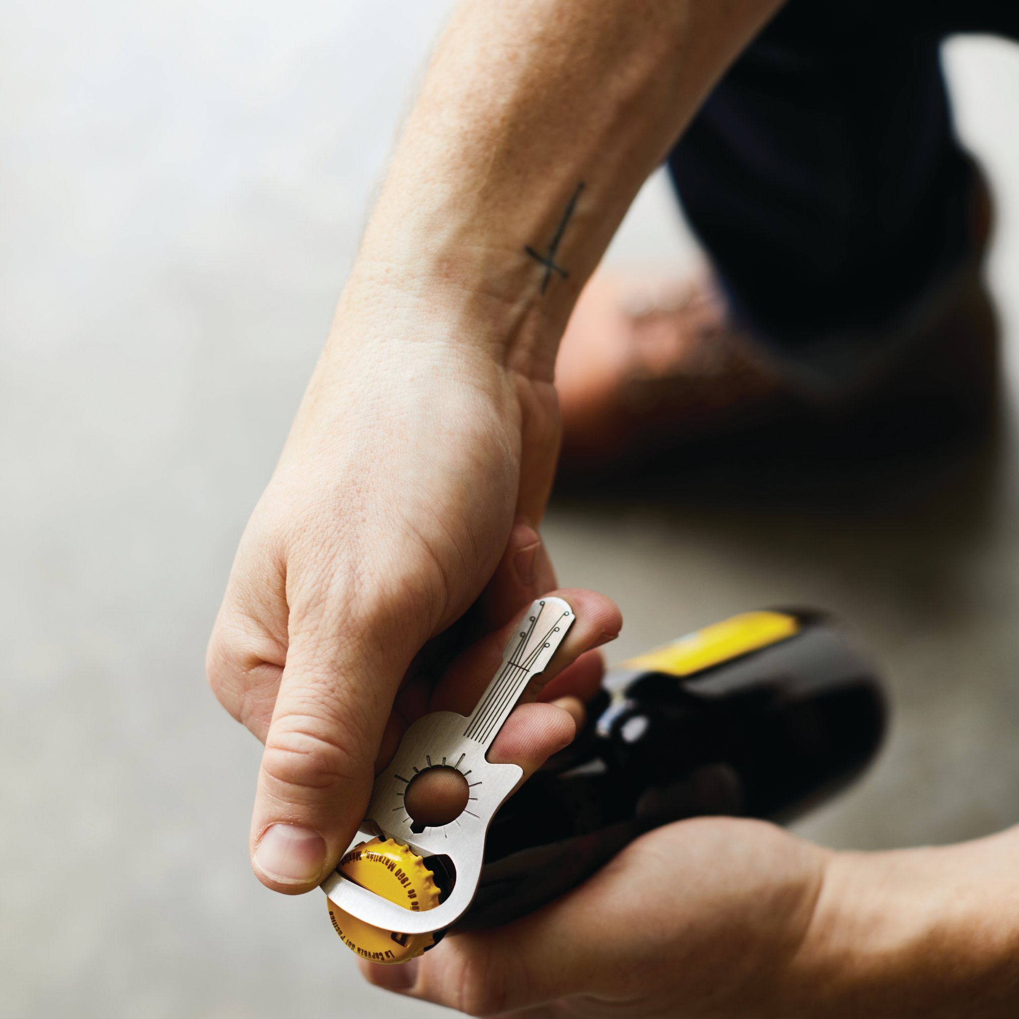 A hand holds the mini guitar bottle opener against a yellow cap on a dark beer bottle