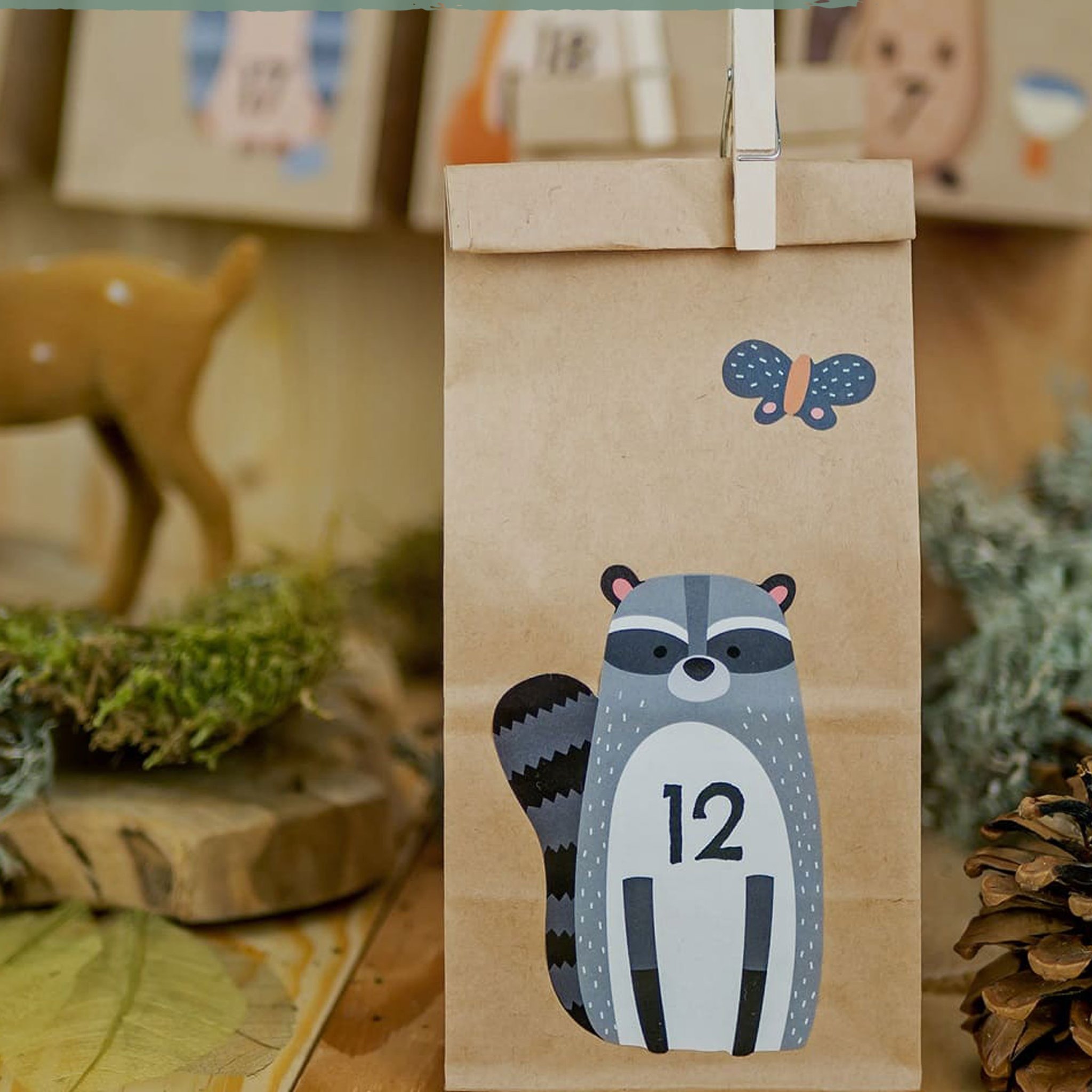 Tüte Nummer 12 mit Waschbär-Aufkleber und Schmetterling, dahinter Rehfigur und Moos