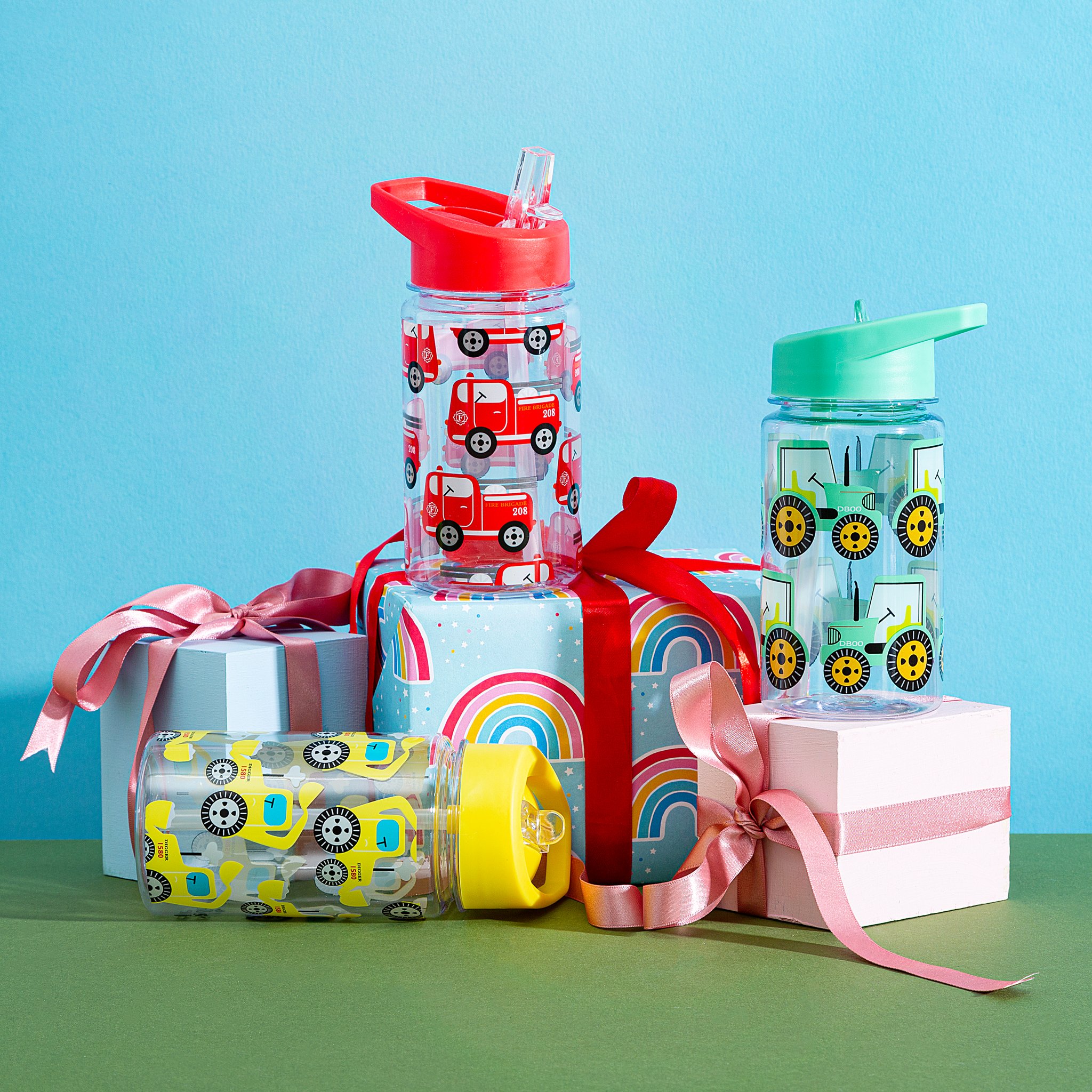 Traktor Kinder-Trinkflasche mit weiteren Kinderflaschen und Geschenken vor blauer Wand