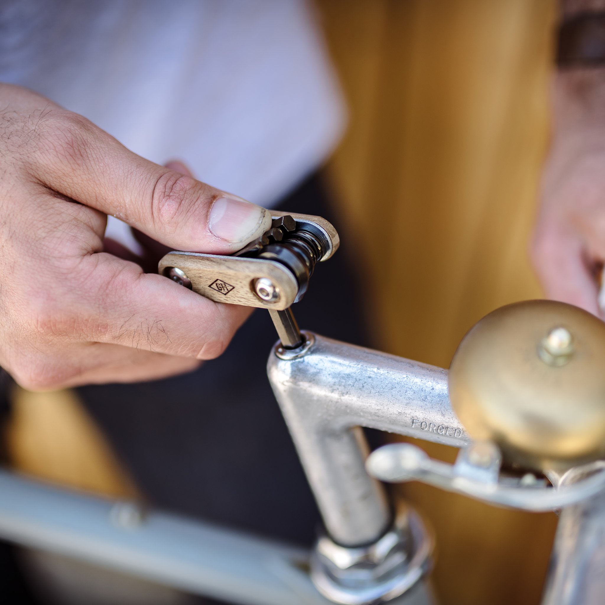 Hand hält das Fahrrad Multitool und dreht mit einem Bit an einer Schraube am Vorbau eines Velos mit Klingel