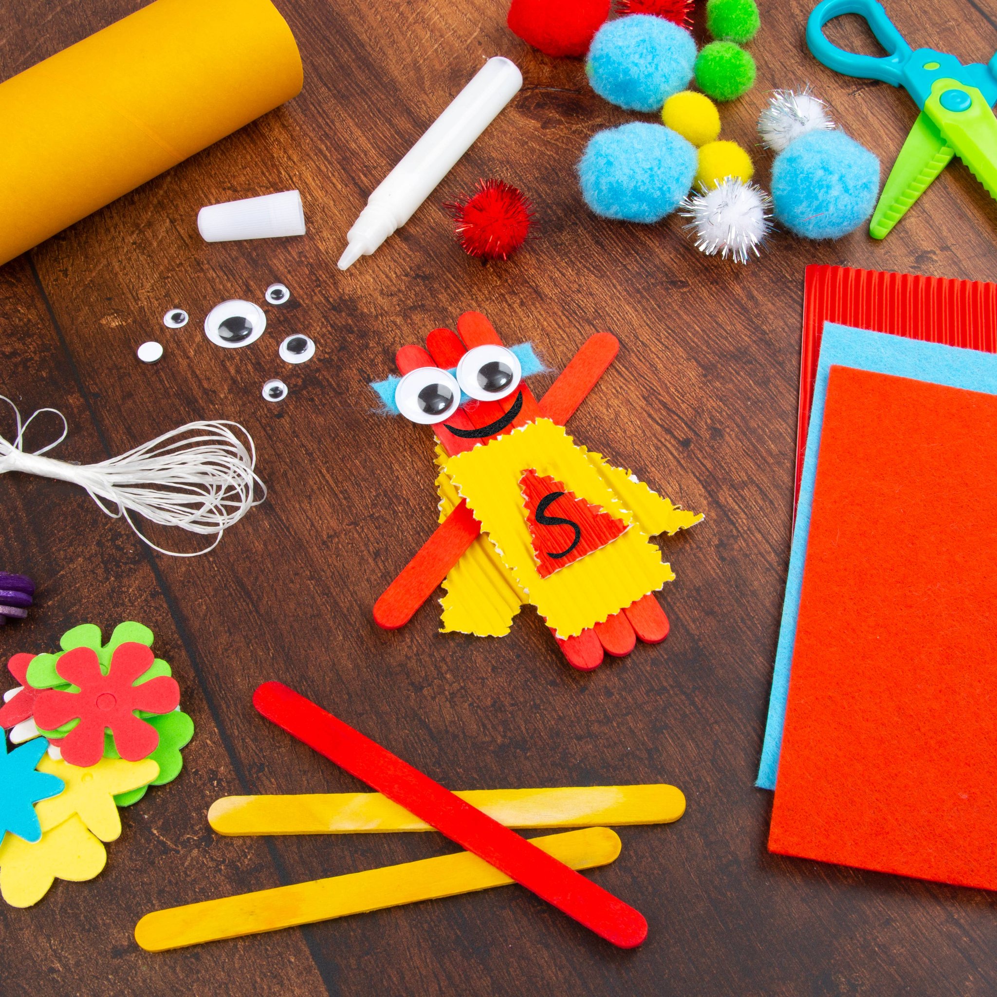 Bastelstäbchen, Pompons, Wackelaugen und Wellpappe auf einem Holztisch ausgebreitet
