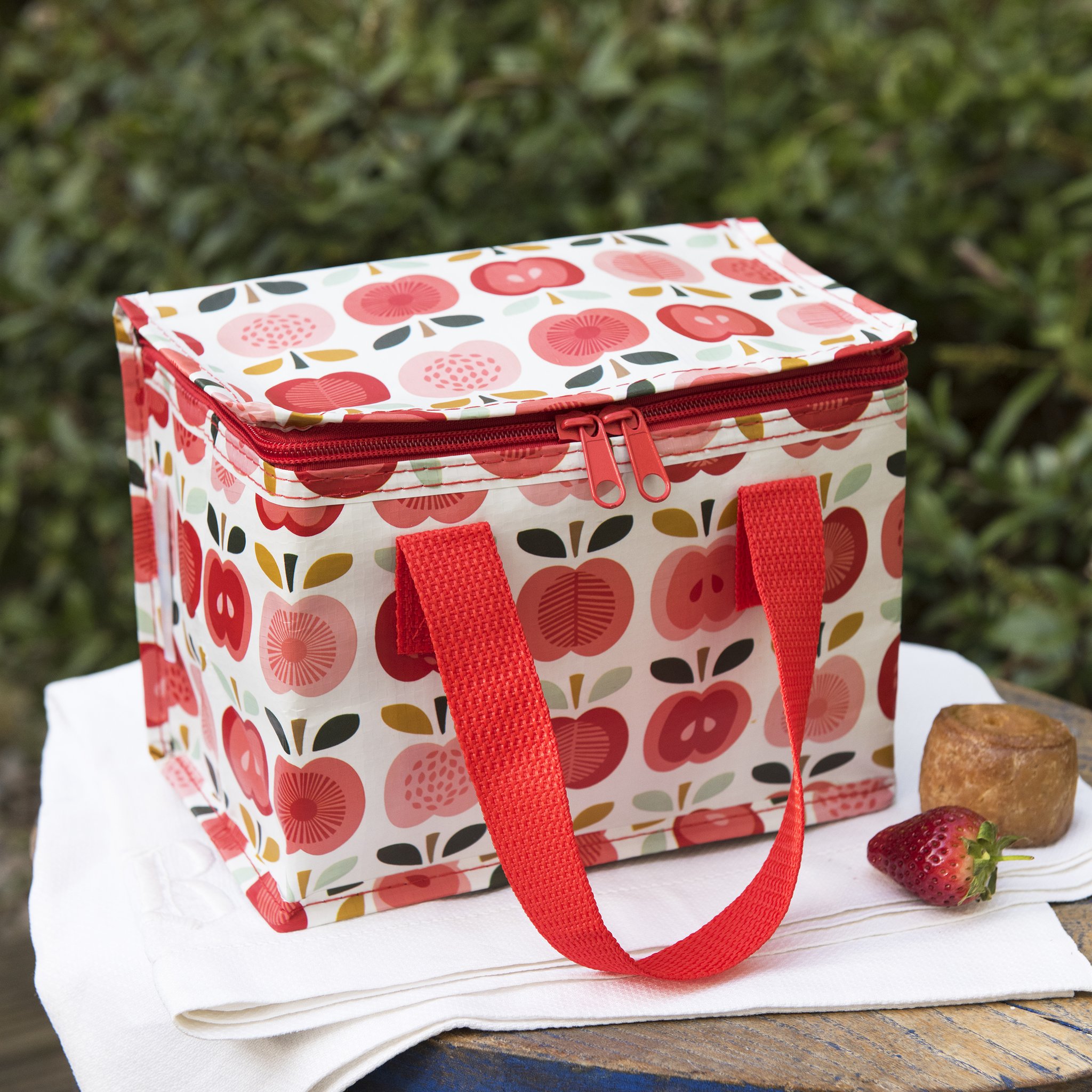 Apfel-Kühltasche auf weissem Tuch mit Erdbeere und Brötchen im Garten