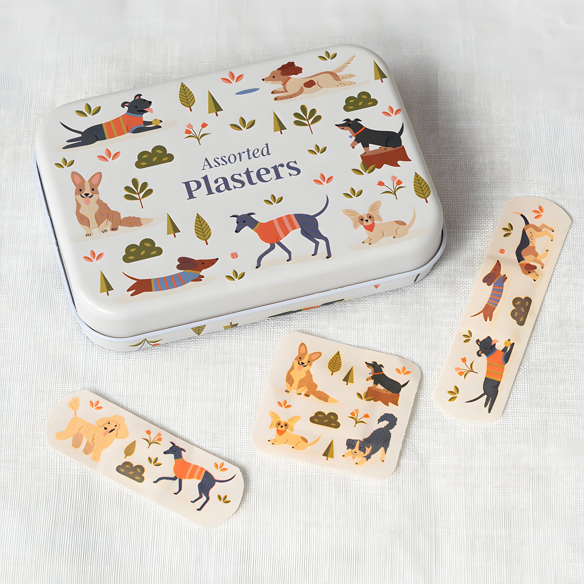 Dose mit Hunde-Pflastern auf hellem Stoff, daneben drei Pflaster mit spielenden Hunden