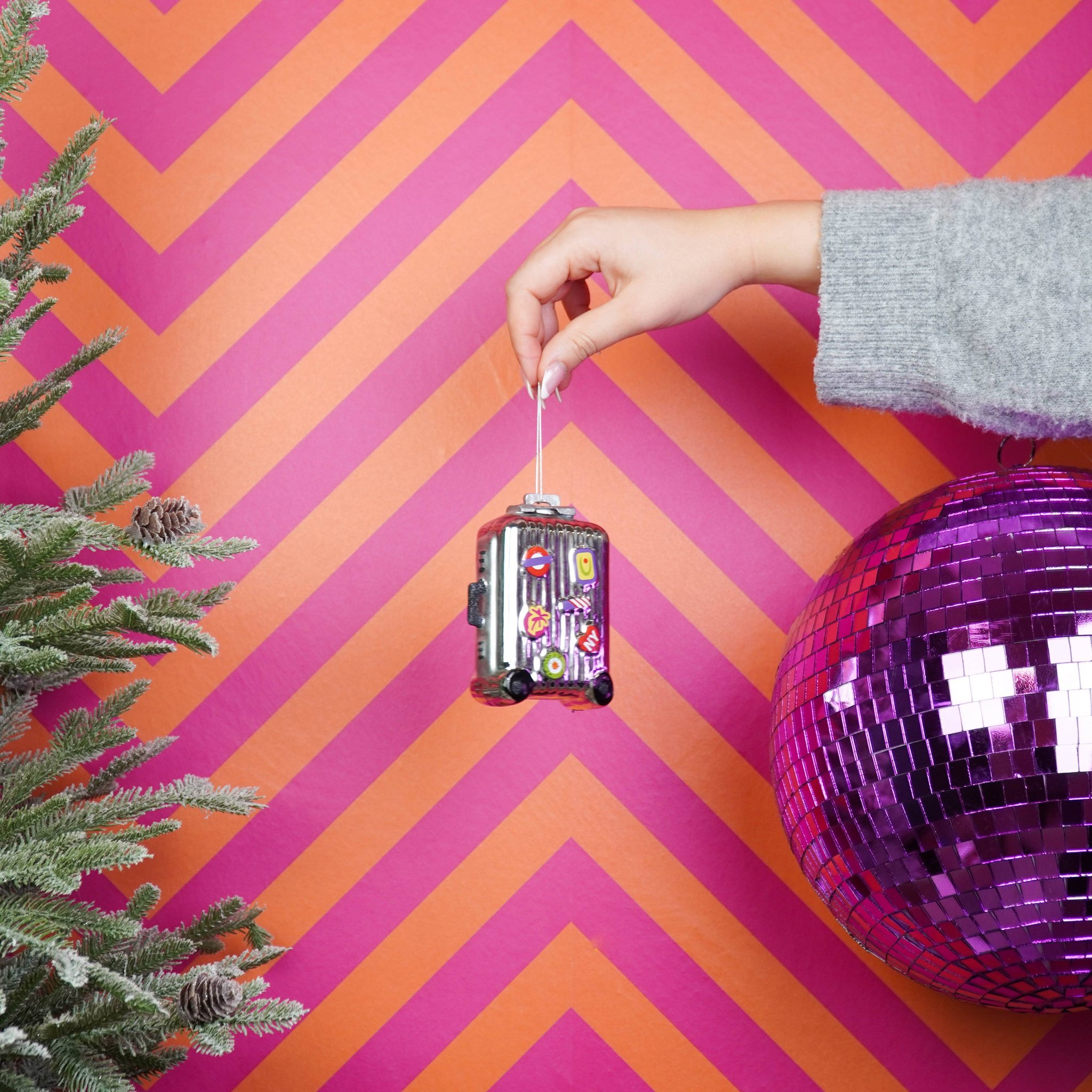 Koffer Weihnachtsanhänger wird vor pinkem Hintergrund mit Discokugel gehalten