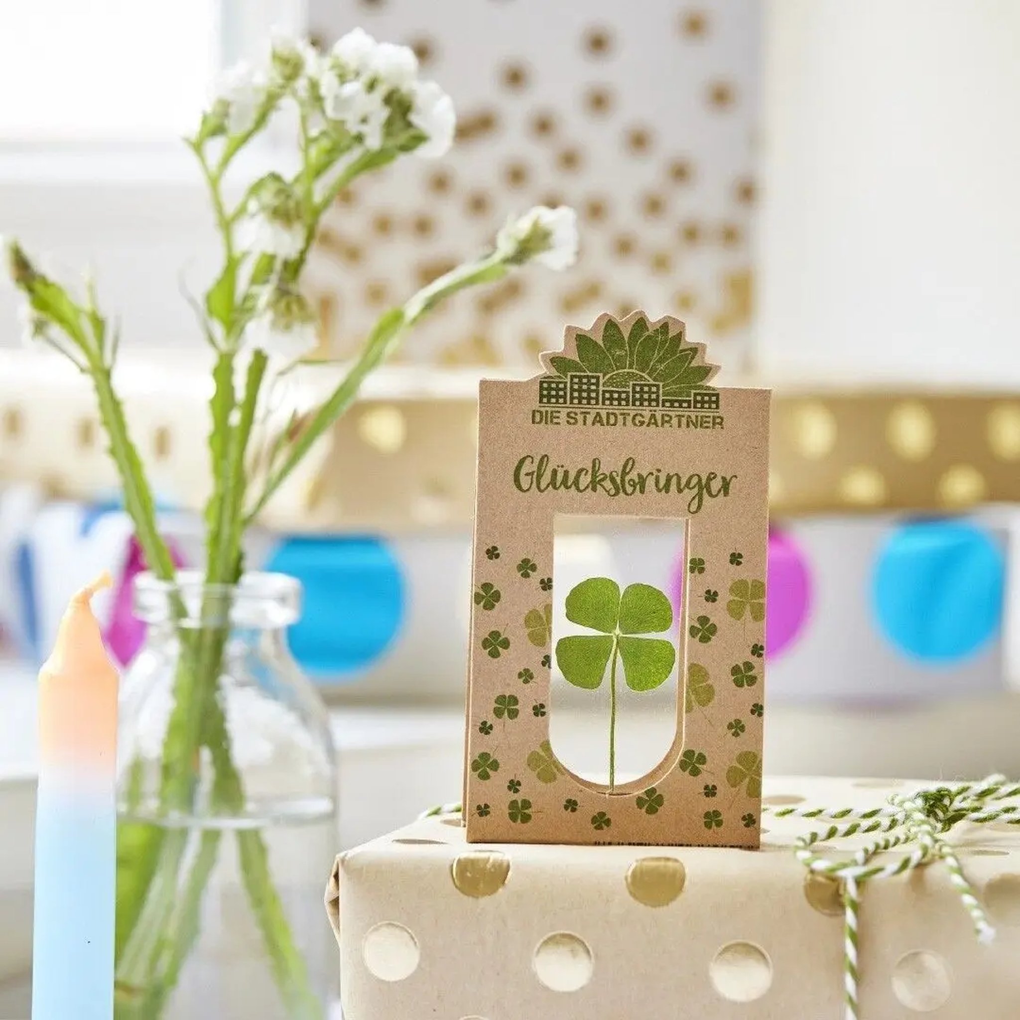 Glücksbringer auf einem Geschenk mit goldenen Punkten neben einer Vase mit Blumen