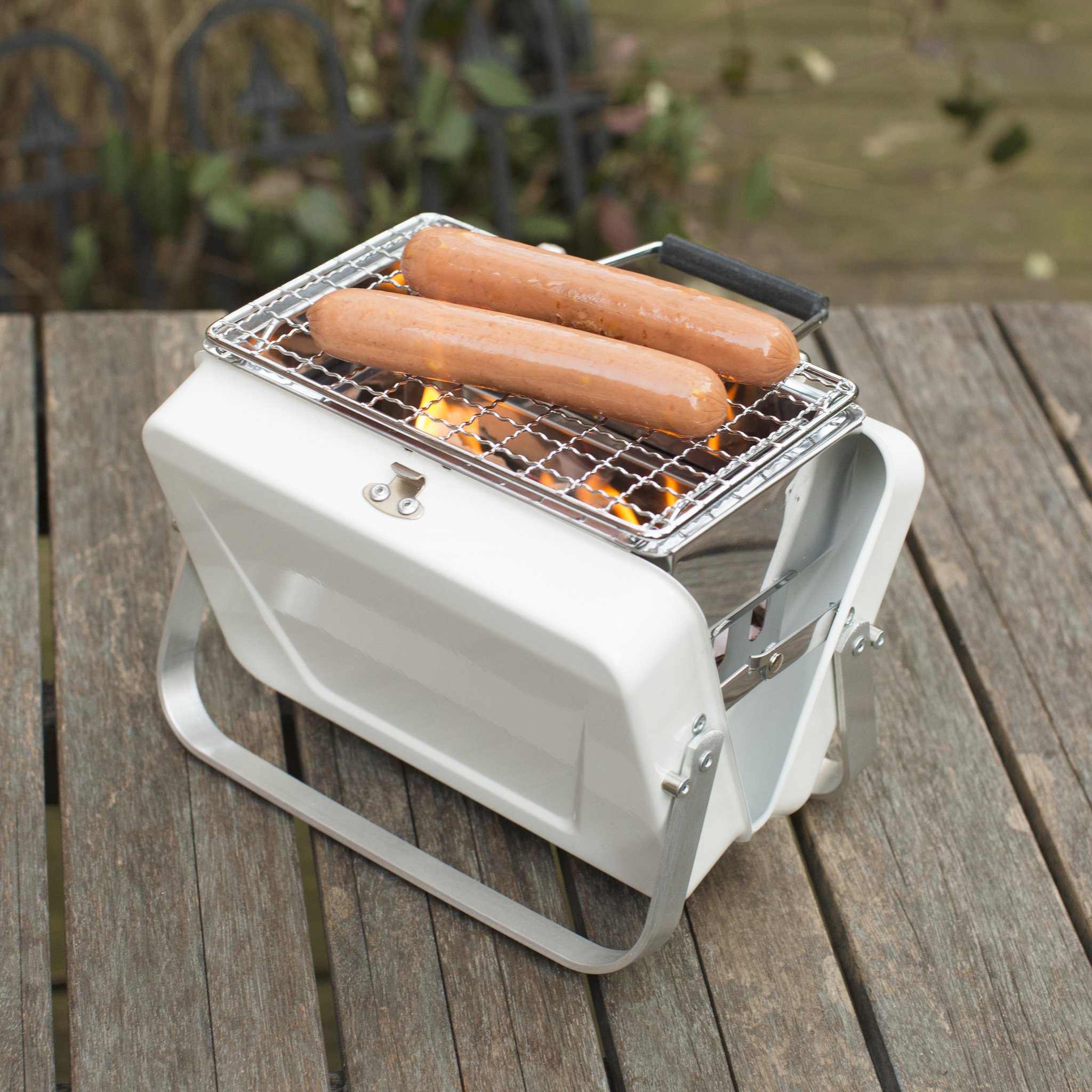 Mini-Koffergrill von Kikkerland – Würste auf Holztisch im Garten