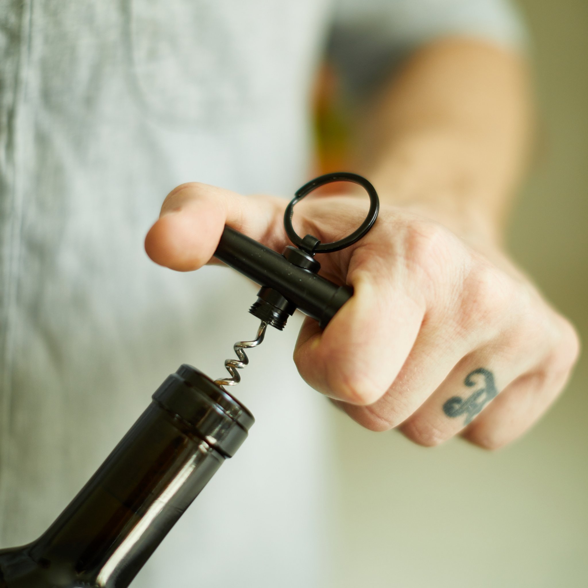 Man holds the keychain corkscrew above a wine bottle, ready to twist it into the cork