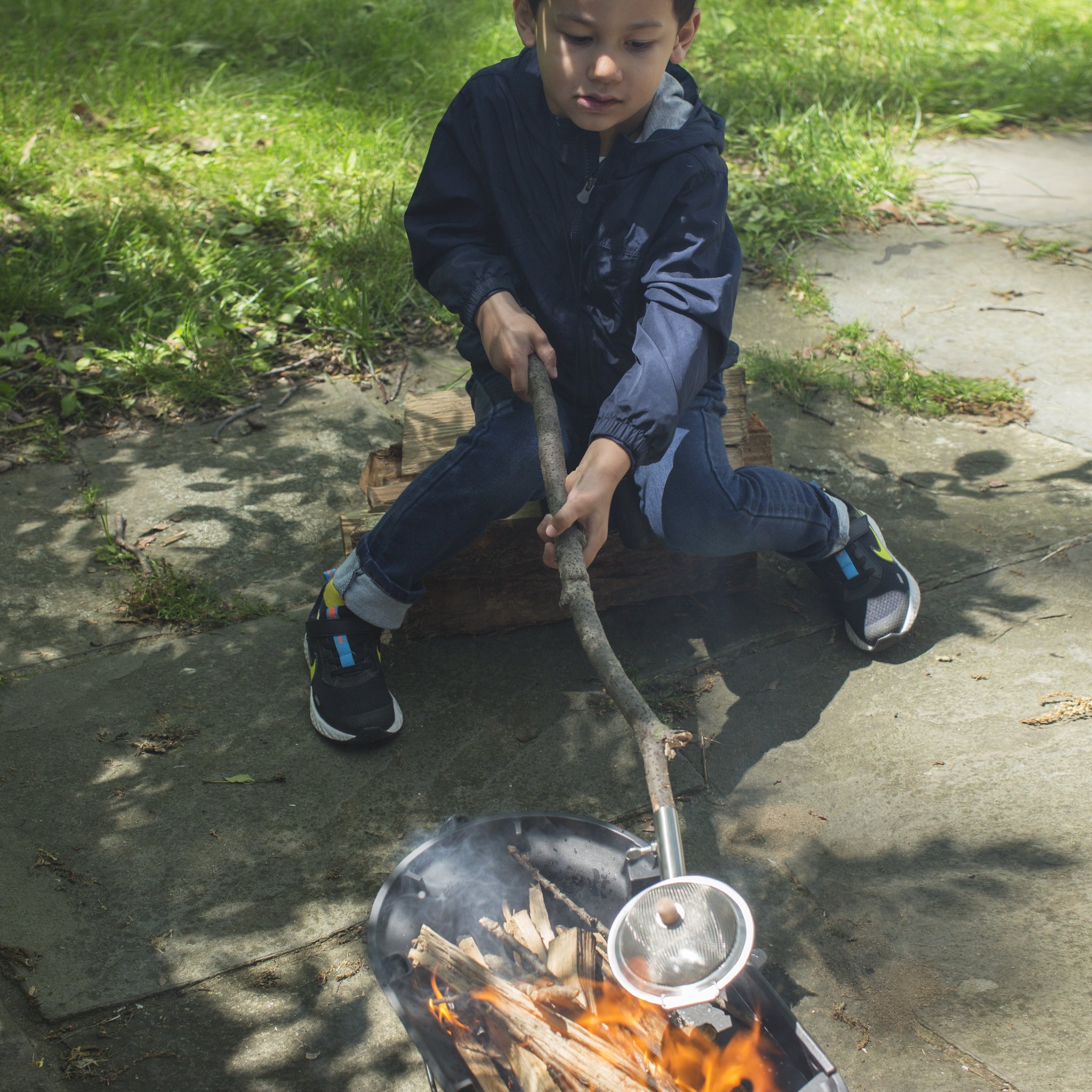 Huckleberry Popcorn-Pfanne – Junge sitzt am Lagerfeuer mit Pfanne am Stock