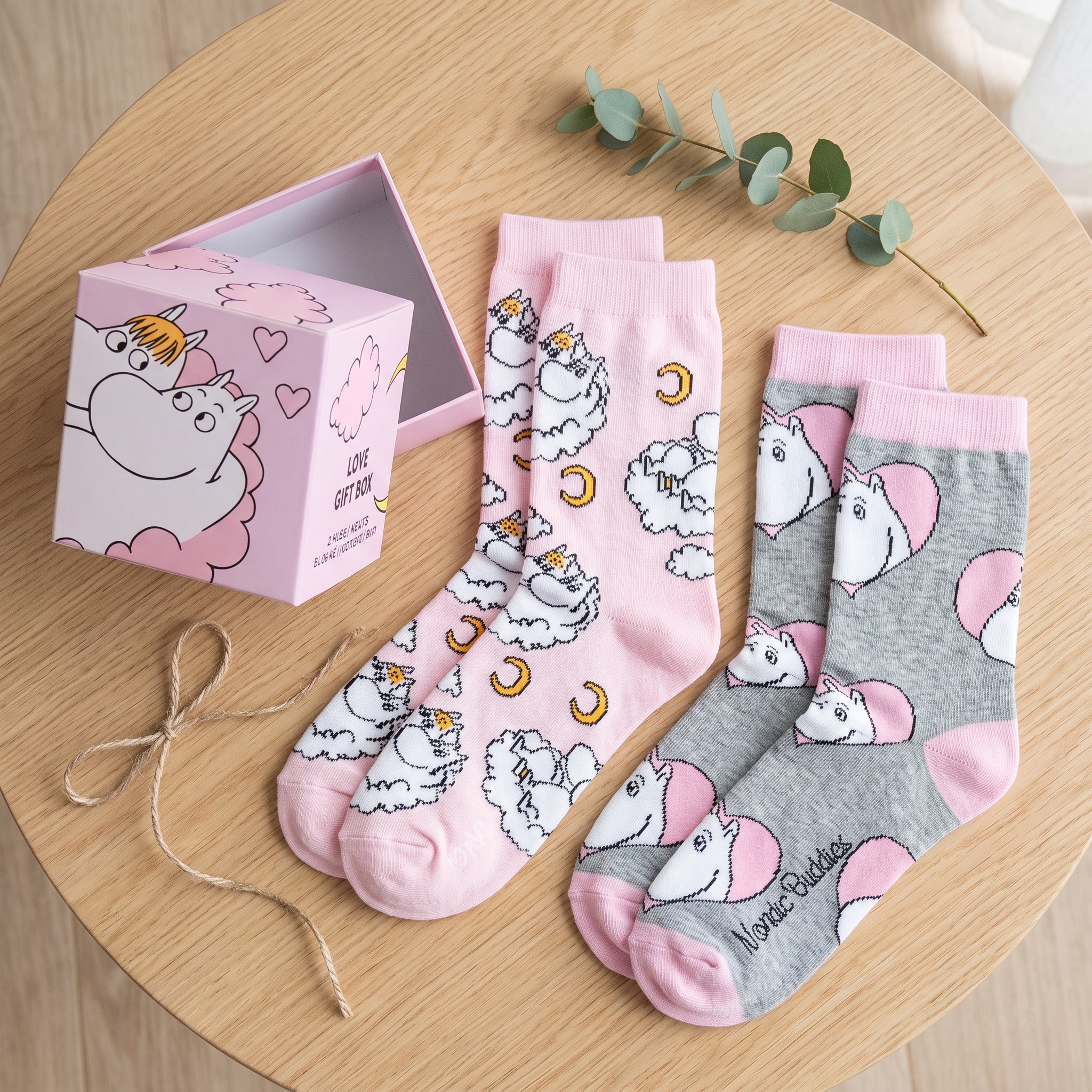 Le due paia di calze Moomin accanto alla scatola regalo rosa su un tavolo di legno