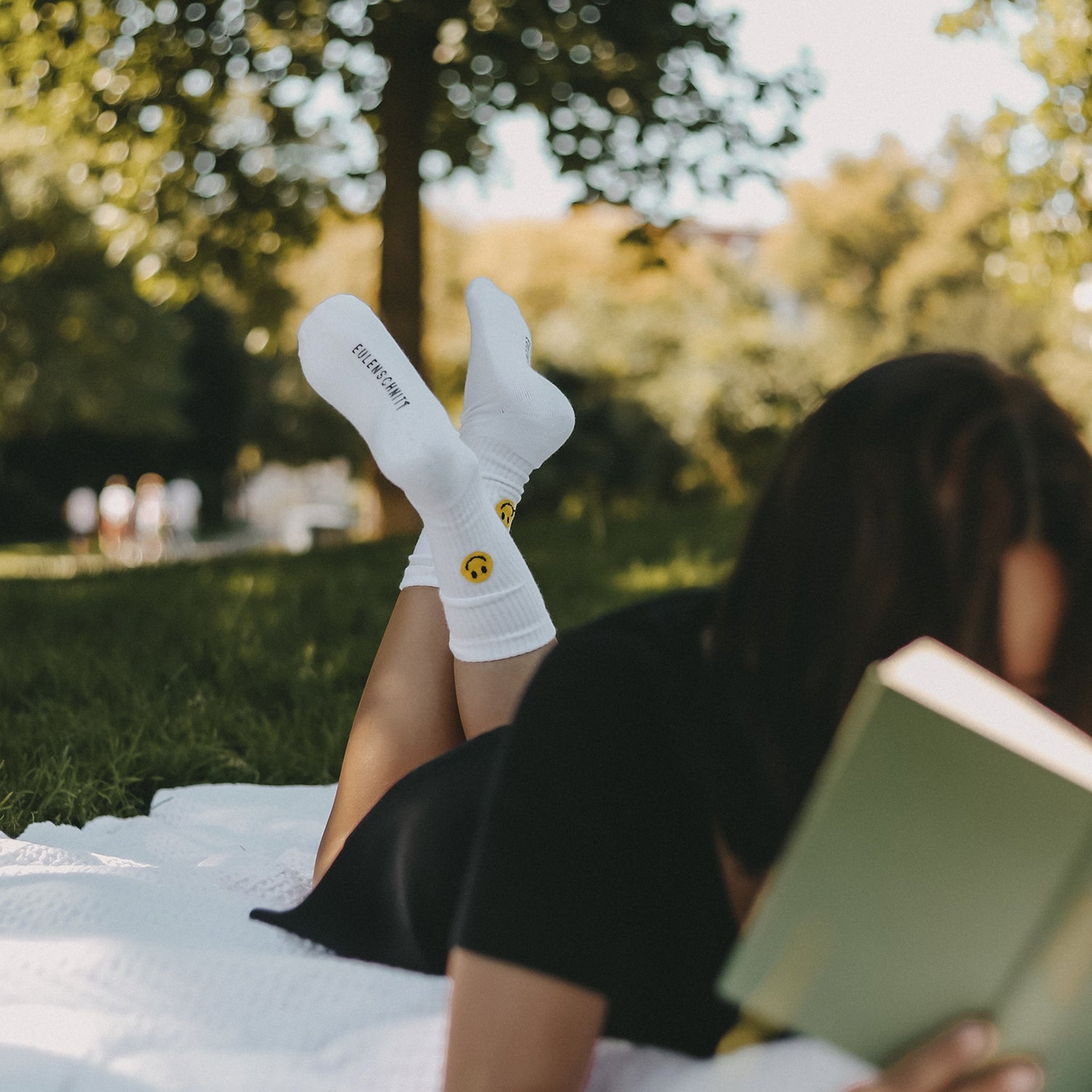 Frau liest auf der Wiese ein Buch, die Füsse in weissen Socken mit gelbem Smiley