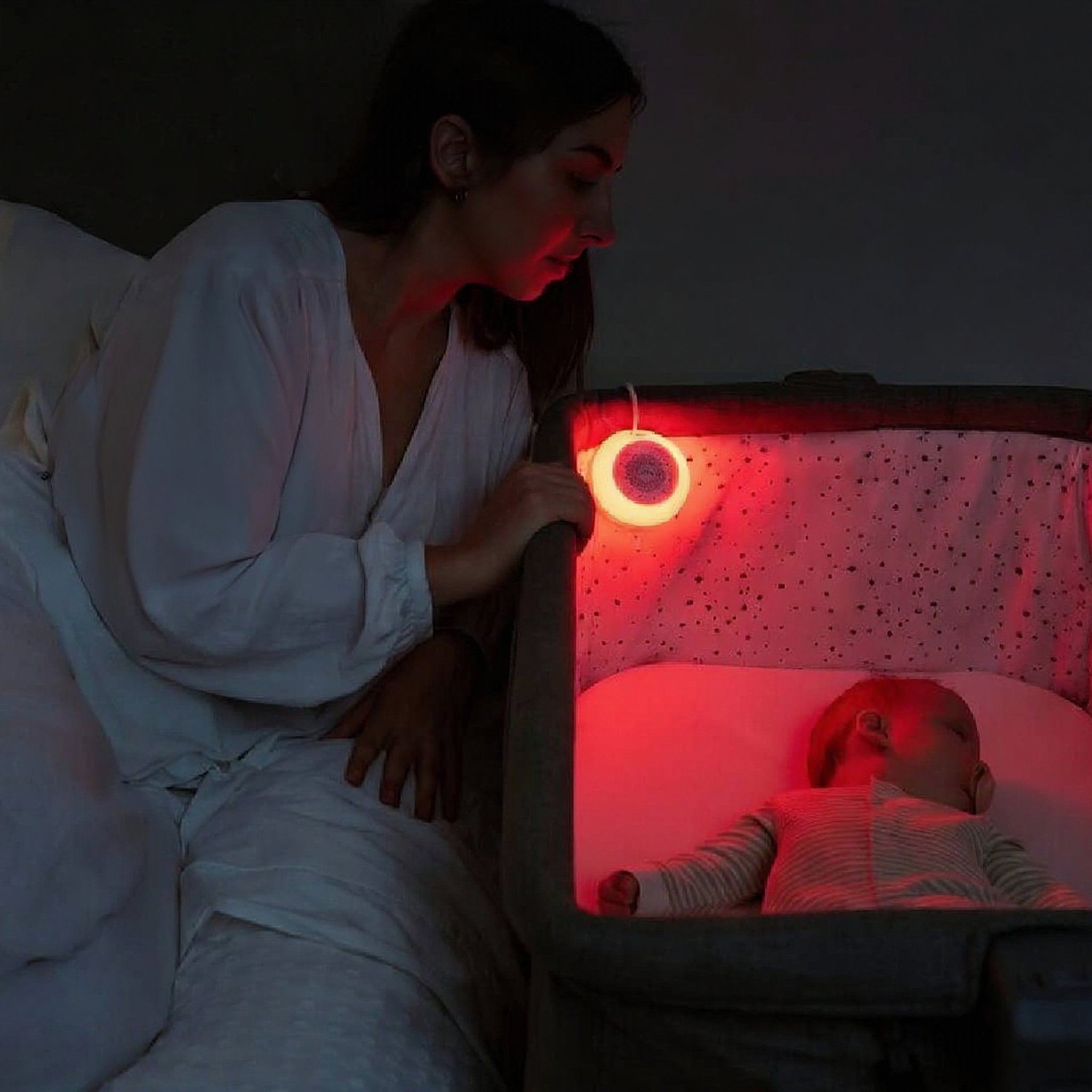Mutter am Babybett mit rotem Schlaflicht der White Noise Maschine