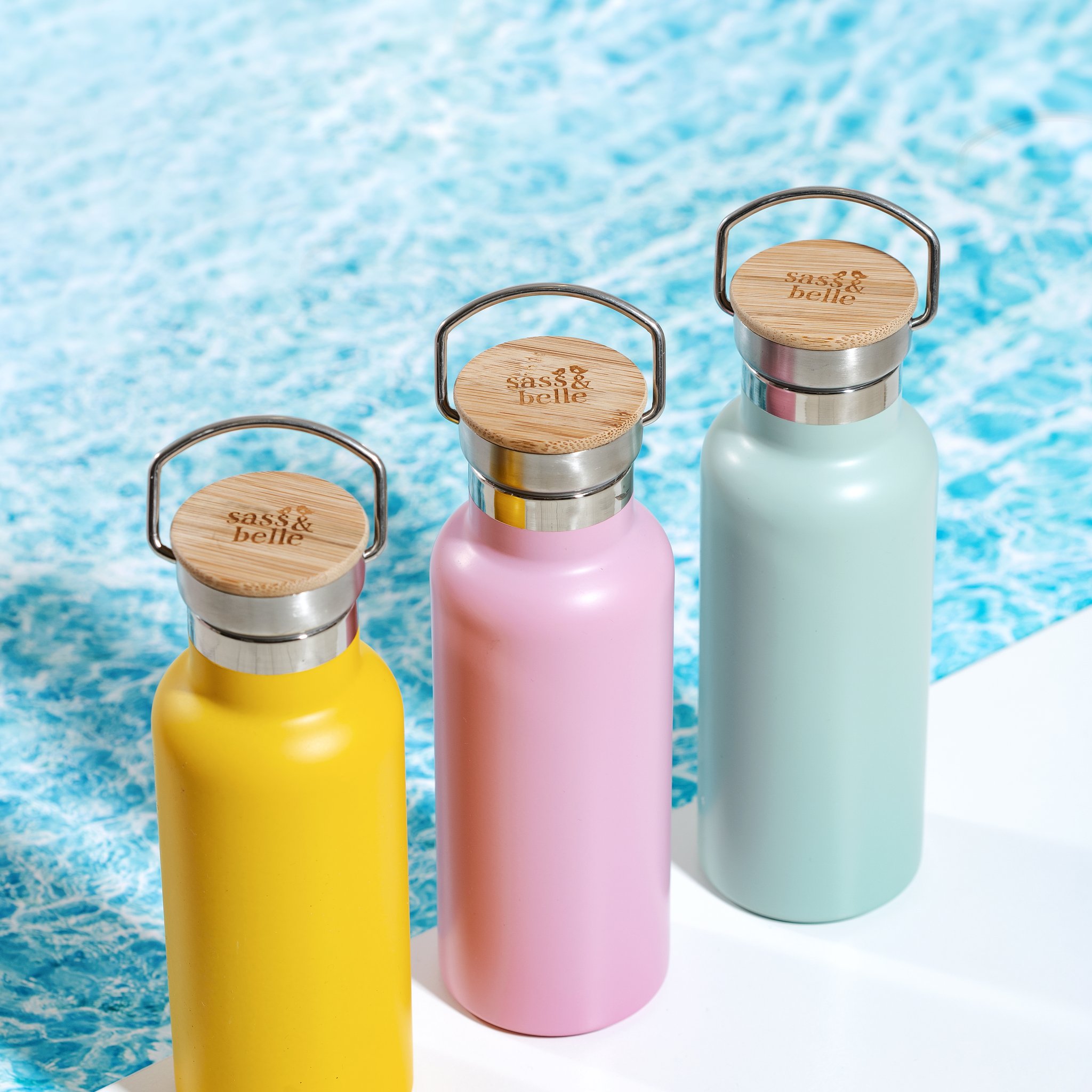 Senfgelbe Wasserflasche mit rosa und mintgrüner Flasche vor Wasser