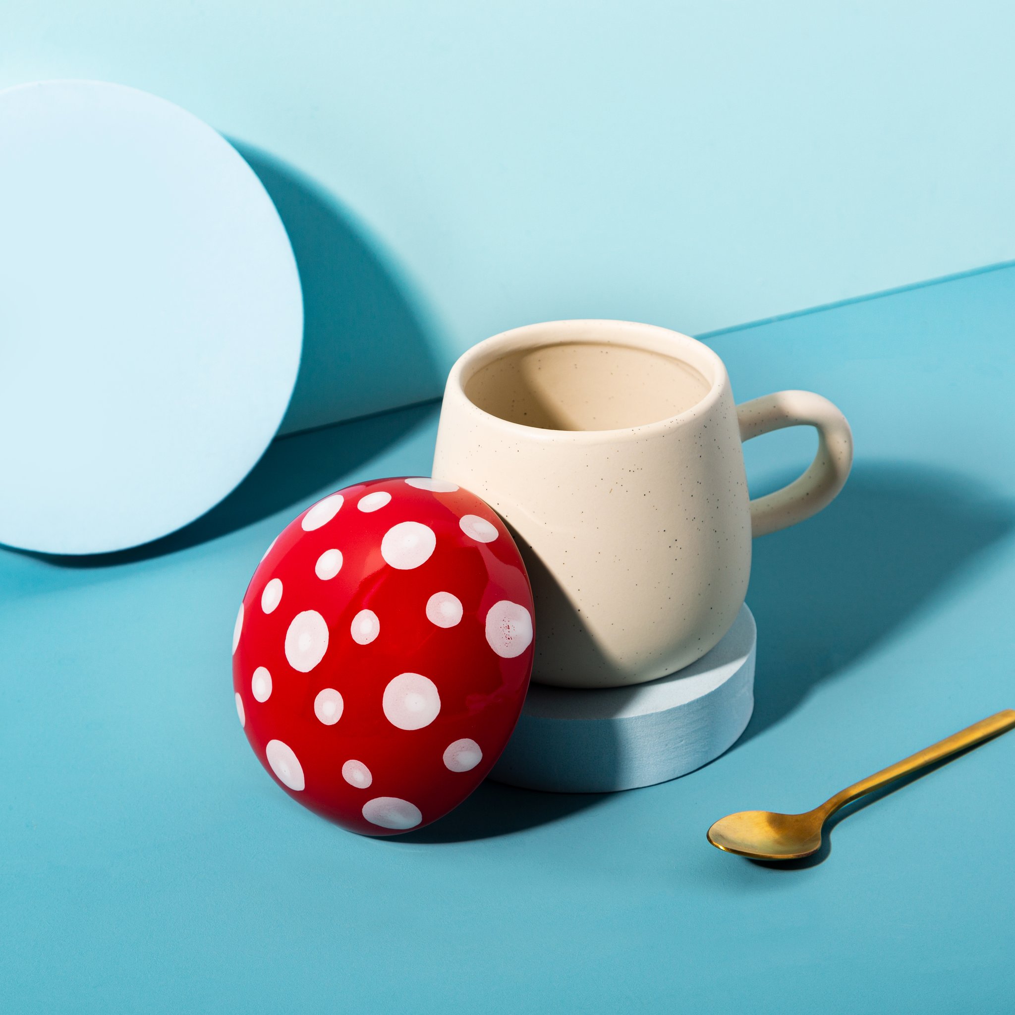 Tasse champignon Sass & Belle avec couvercle champignon retiré et cuillère dorée sur fond bleu