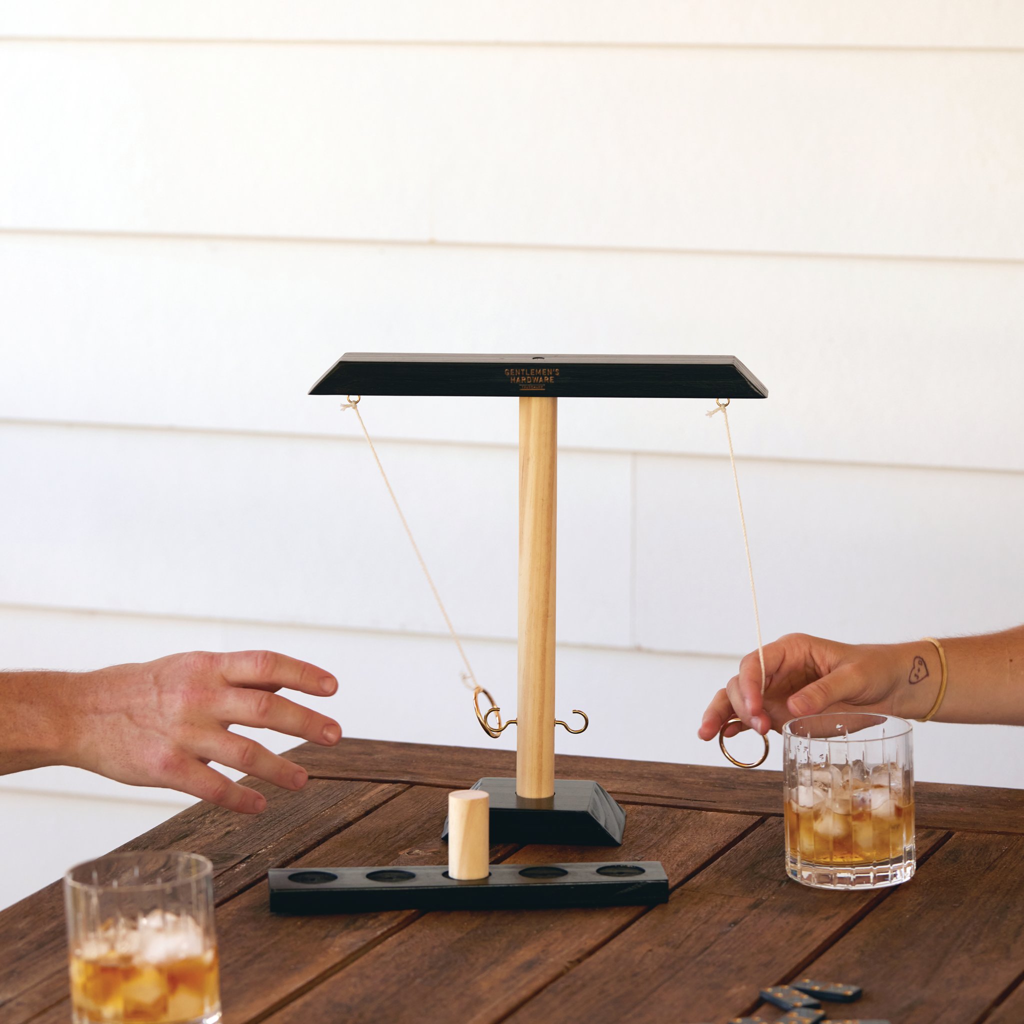 Deux joueurs à une table en bois avec le Jeu de Lancer d'Anneau, un anneau en mouvement et un verre de chaque côté