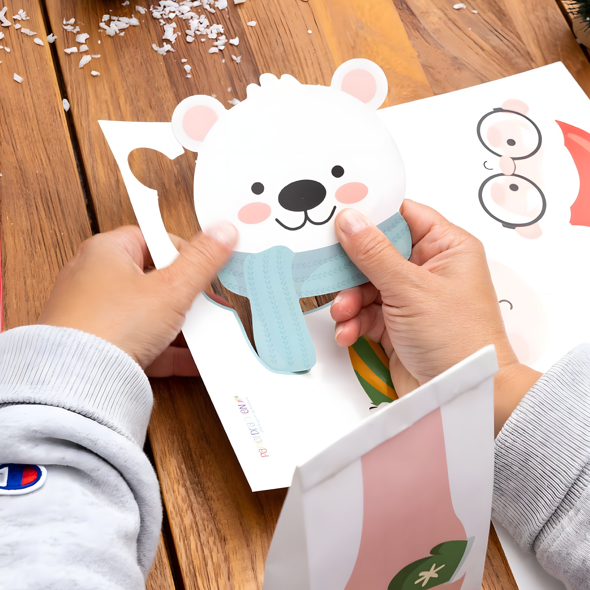 Hände setzen das Eisbär-Gesicht aus dem Stanzbogen auf eine Tüte des Weihnachtshelfer Adventskalenders