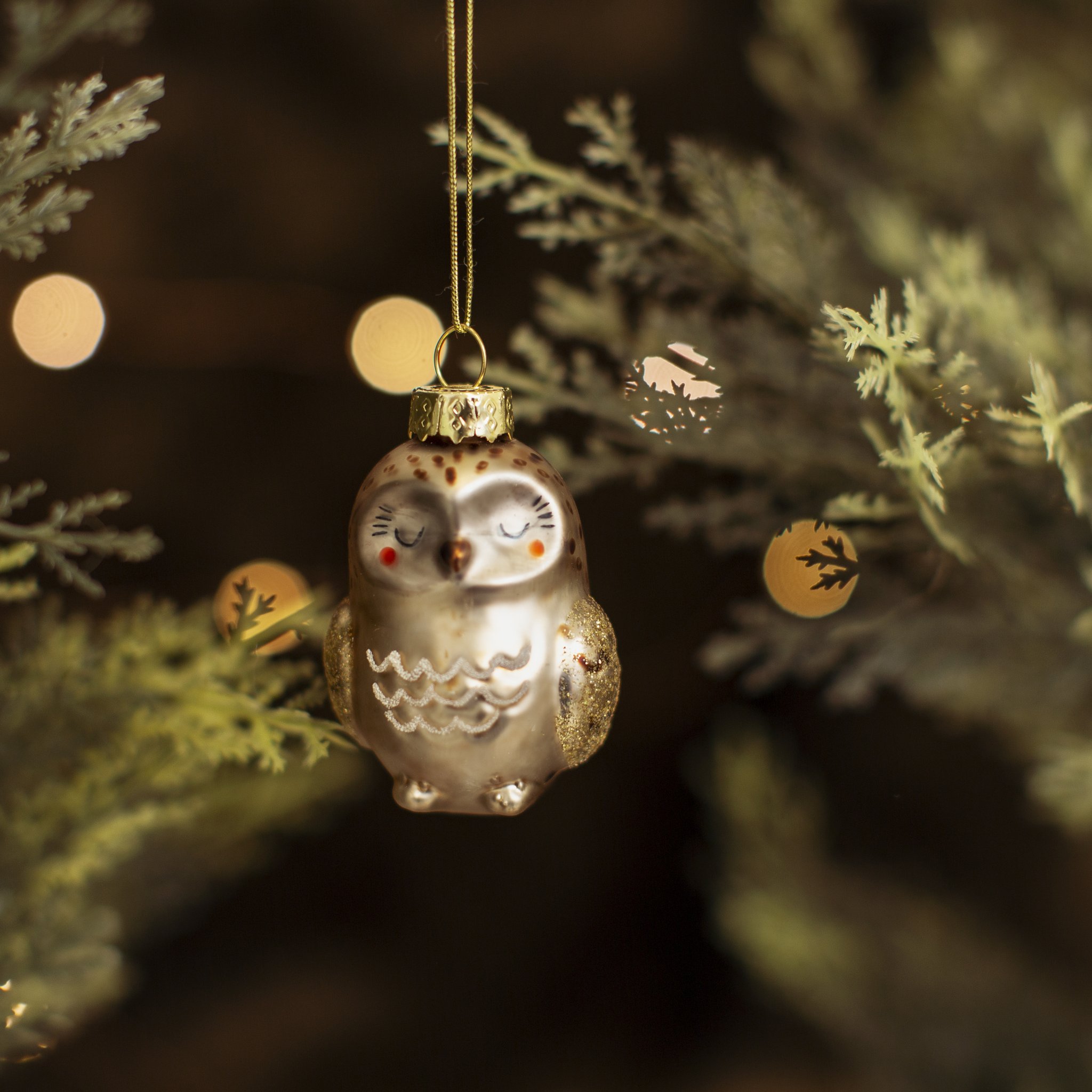 Décoration de sapin hibou Sass & Belle en verre sur une branche de sapin avec bokeh doré