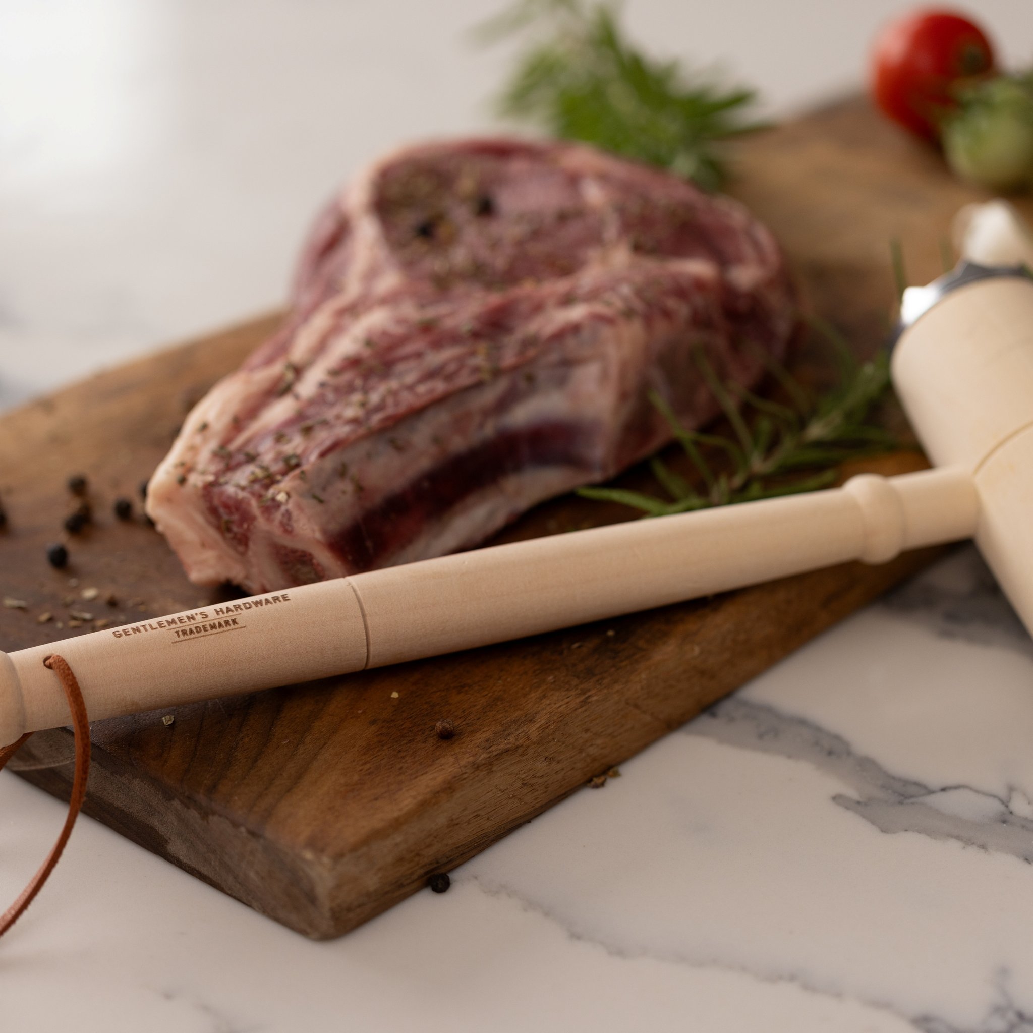Close-up of the wooden handle with Gentlemen's Hardware branding, a seasoned steak on the board behind it