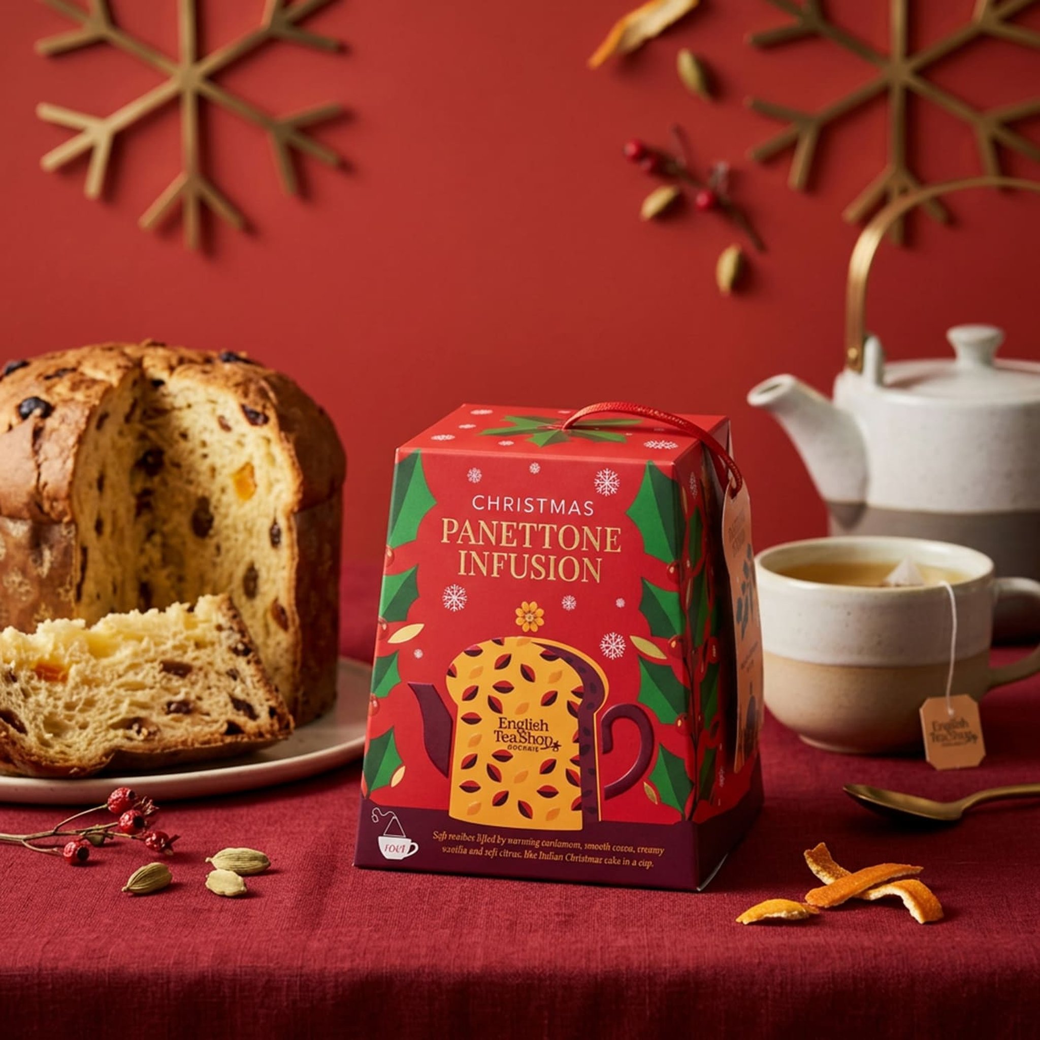 Panettone tea box on a red tablecloth beside a sliced panettone, teapot and cup of tea
