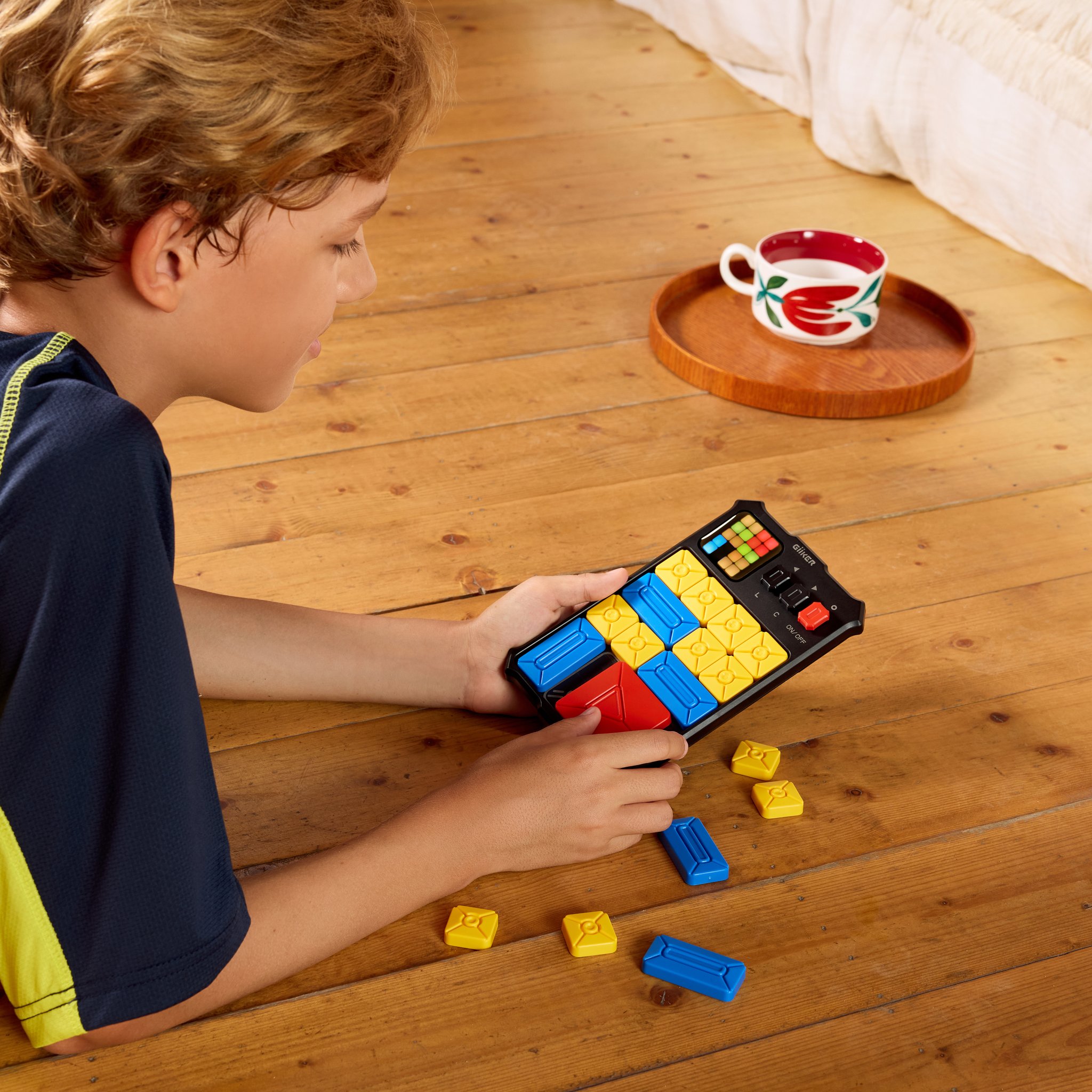 Ein Junge schiebt am Tischchen die Blöcke auf dem Schiebe-Puzzle Super Slide, lose Spielsteine daneben.