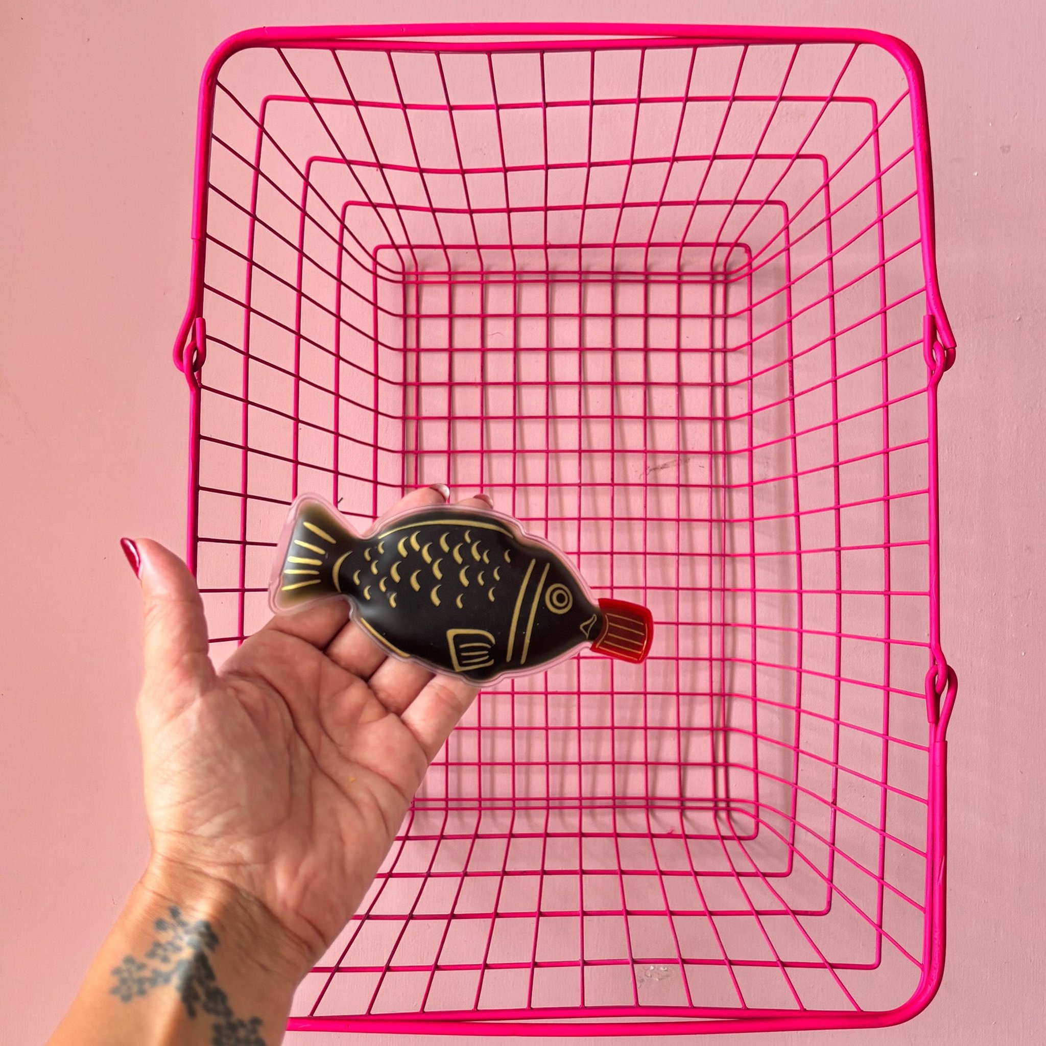 Hand holding the fish-shaped soy sauce hand warmer in front of a pink basket