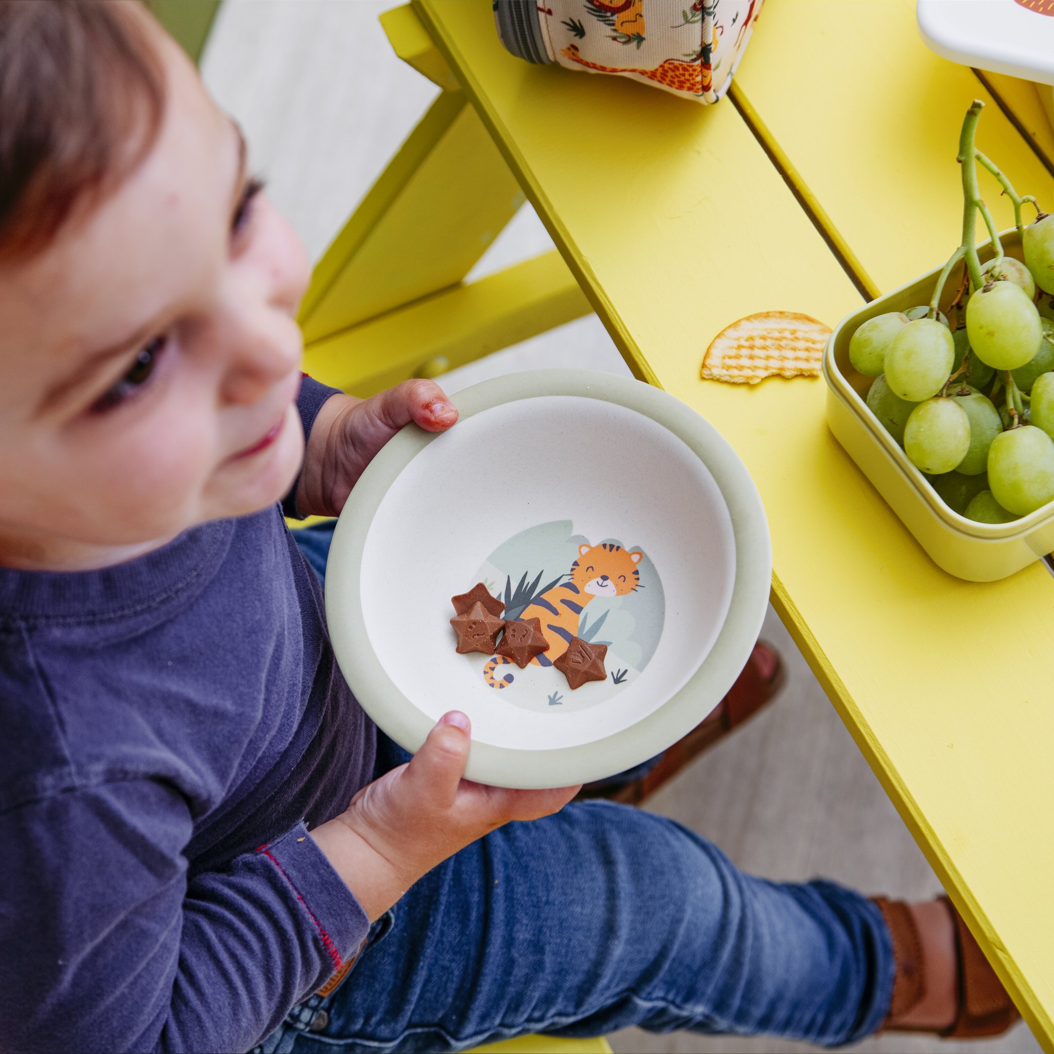 Bambino che tiene la ciotola Savannah Safari a un tavolo da picnic giallo
