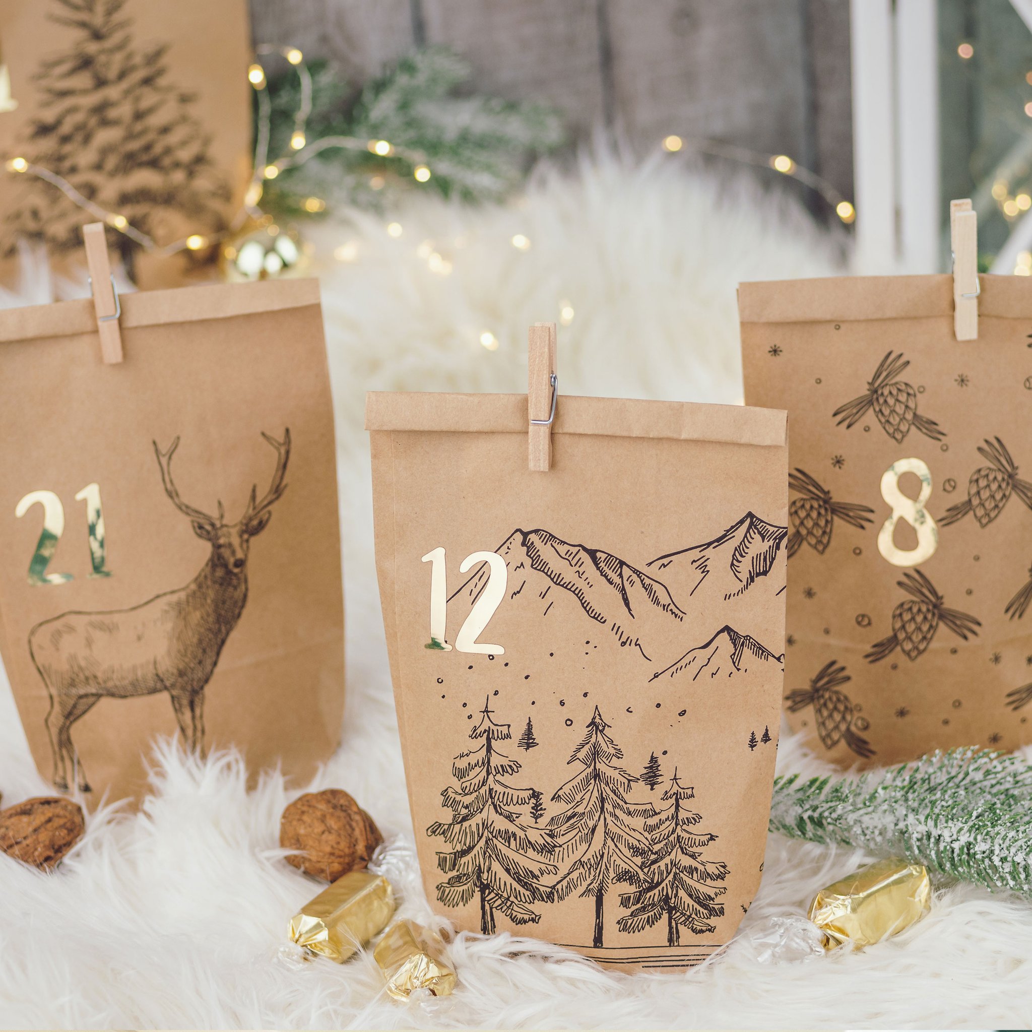 Drei Tüten mit den Zahlen 21, 12 und 8, Berg- und Tannenmotiv, Lichterkette im Hintergrund
