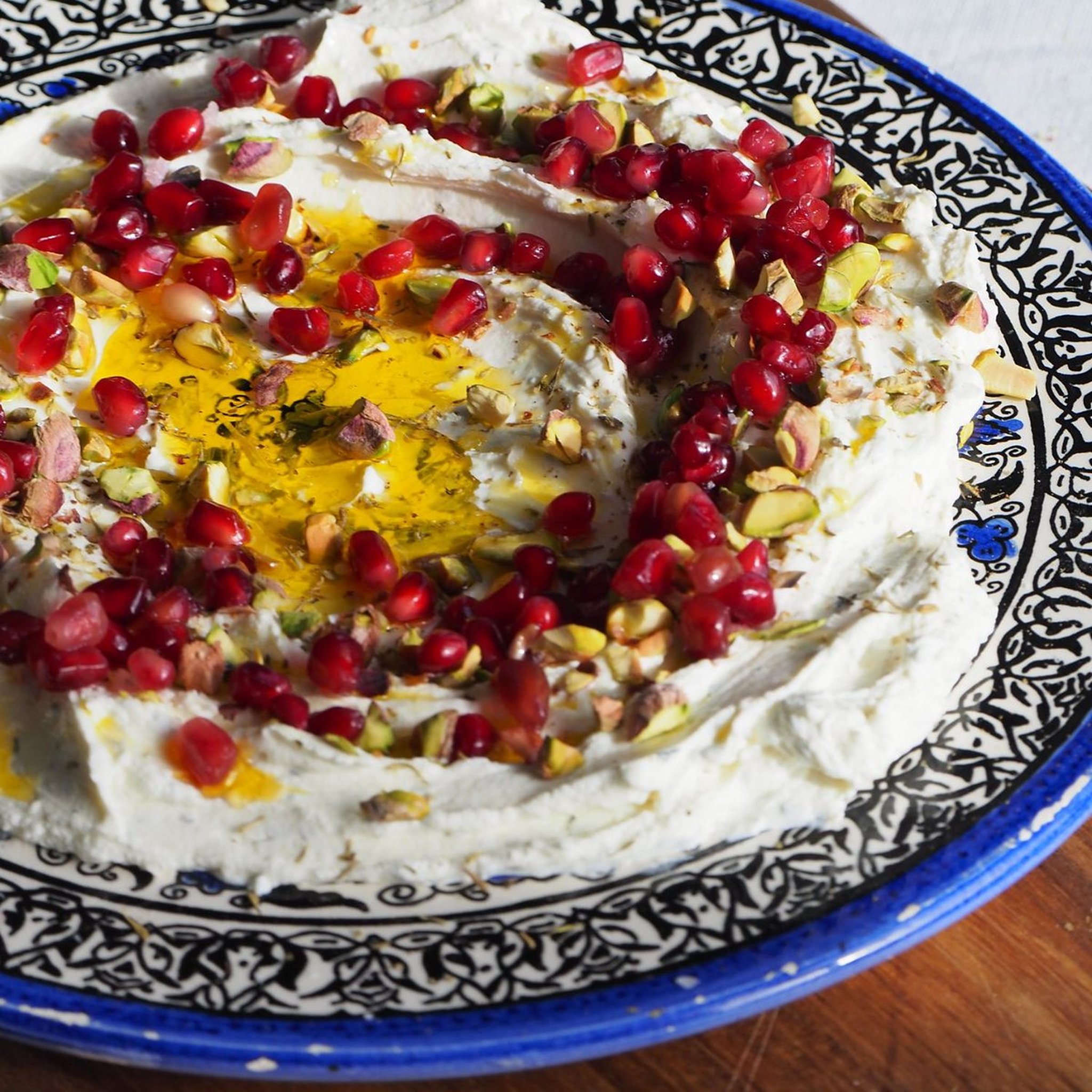 Selbstgemachter Labneh mit Granatapfelkernen, Pistazien und Olivenöl auf einem Keramikteller