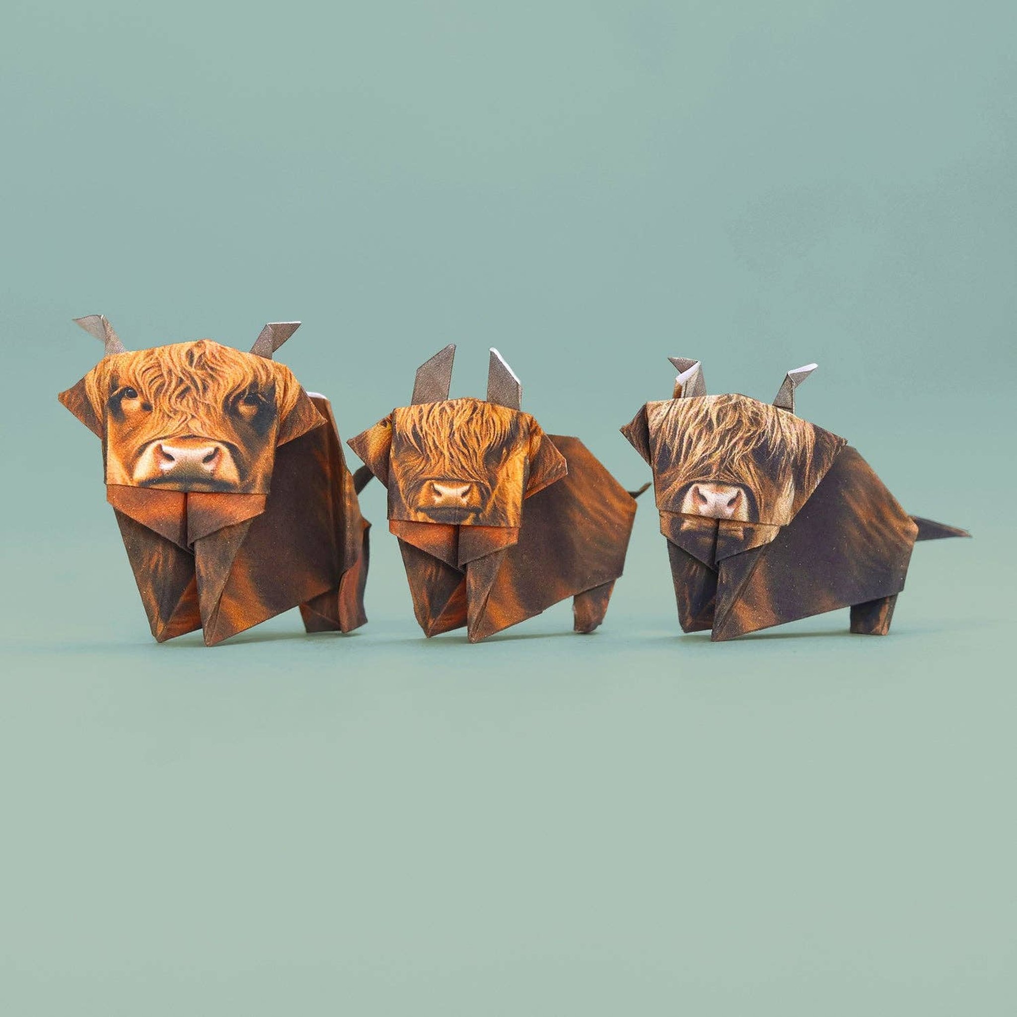 Three folded paper Highland cows side by side on a mint background