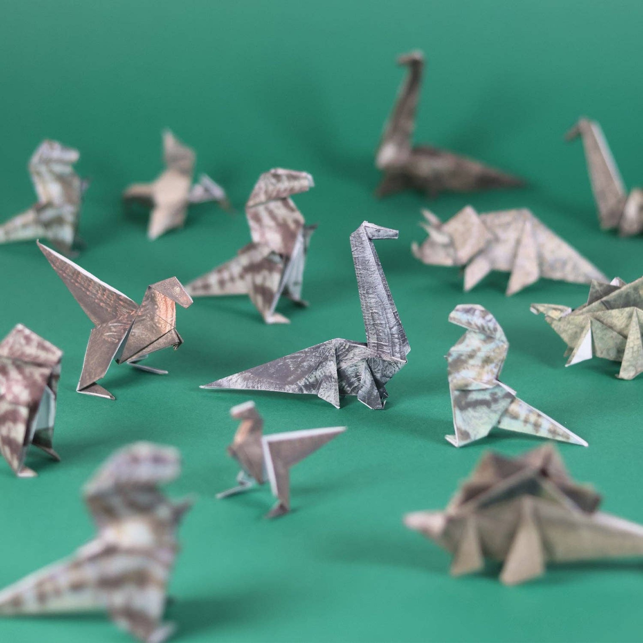Lots of folded origami dinosaurs such as T-Rex and Stegosaurus on a green background