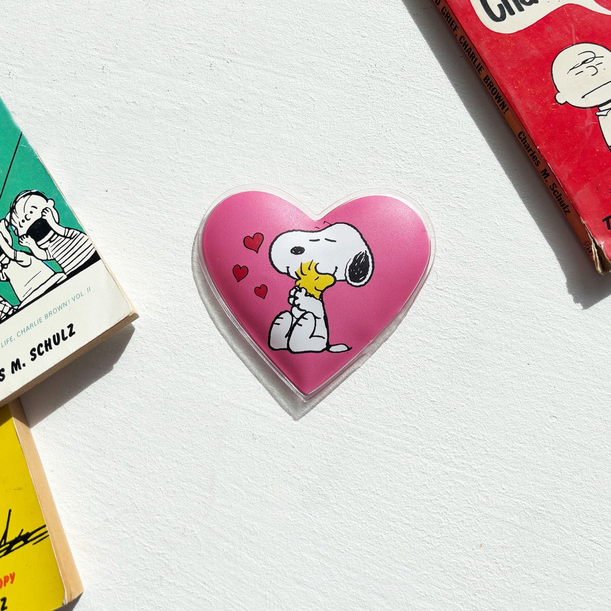 Pinker Herz-Handwärmer mit Snoopy neben Peanuts-Büchern
