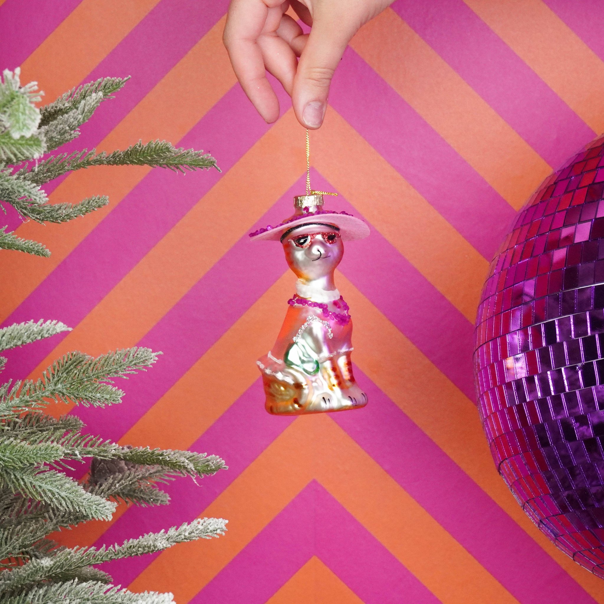 Diva-Katze Weihnachtsanhänger mit rosa Hut wird vor pinkem Hintergrund gehalten