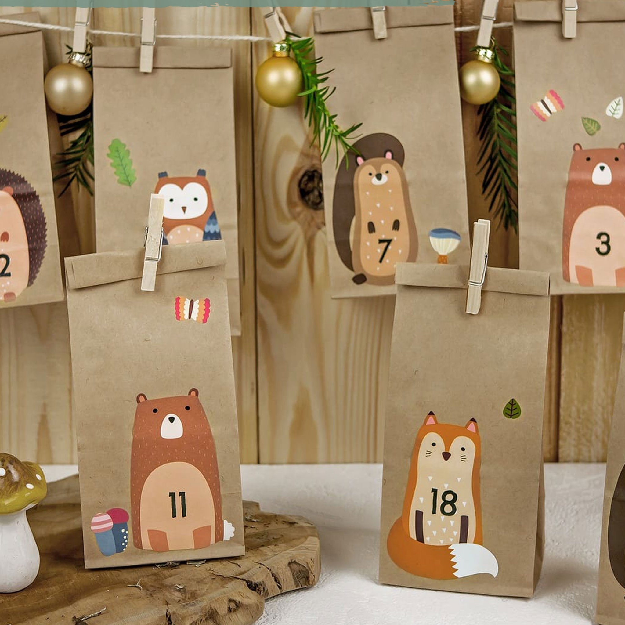 Papiertüten mit Igel, Eule, Eichhörnchen und Bär hängen mit Holzklammern an einer Schnur vor der Holzwand