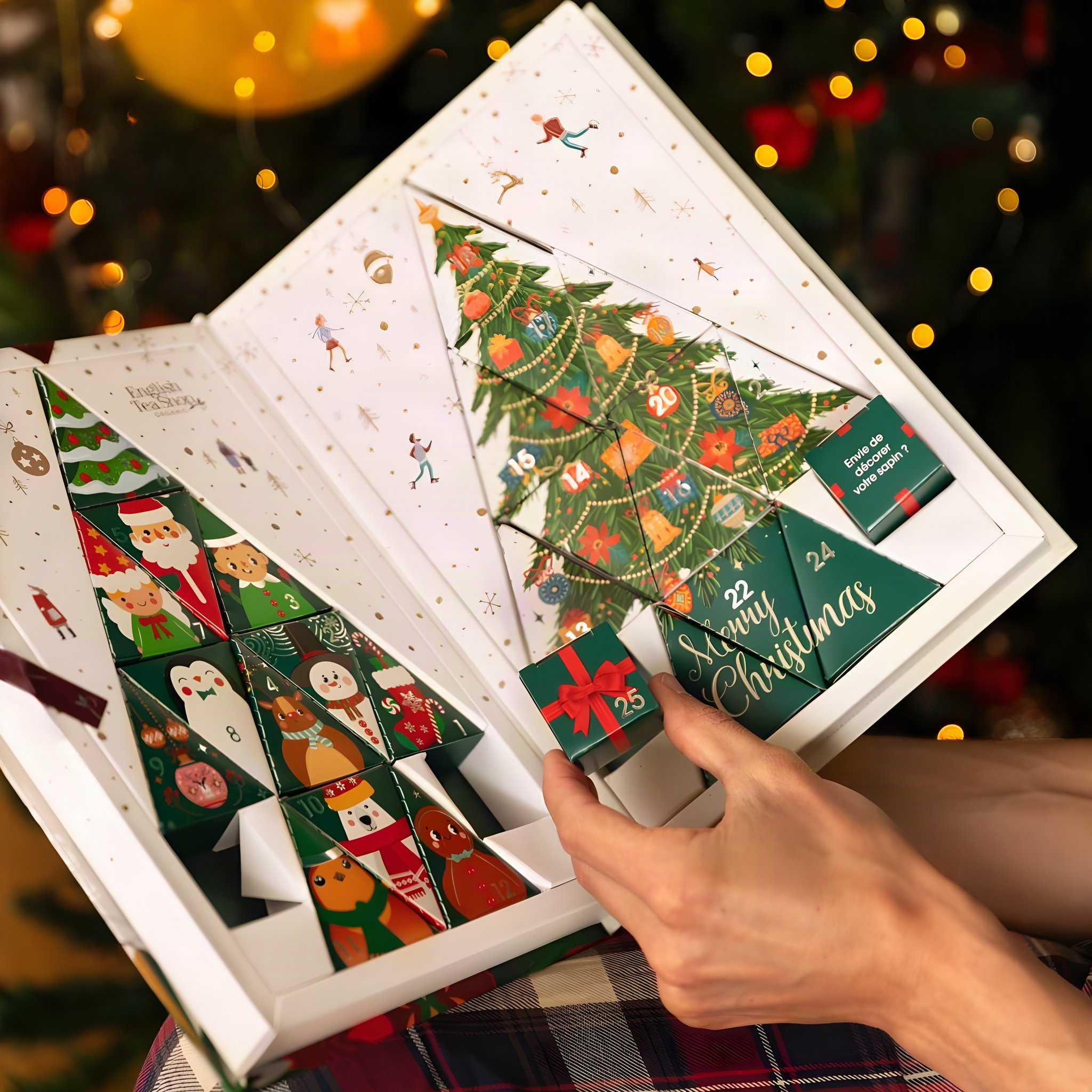 Hand taking a small gift box from the opened tea advent calendar in front of twinkling lights