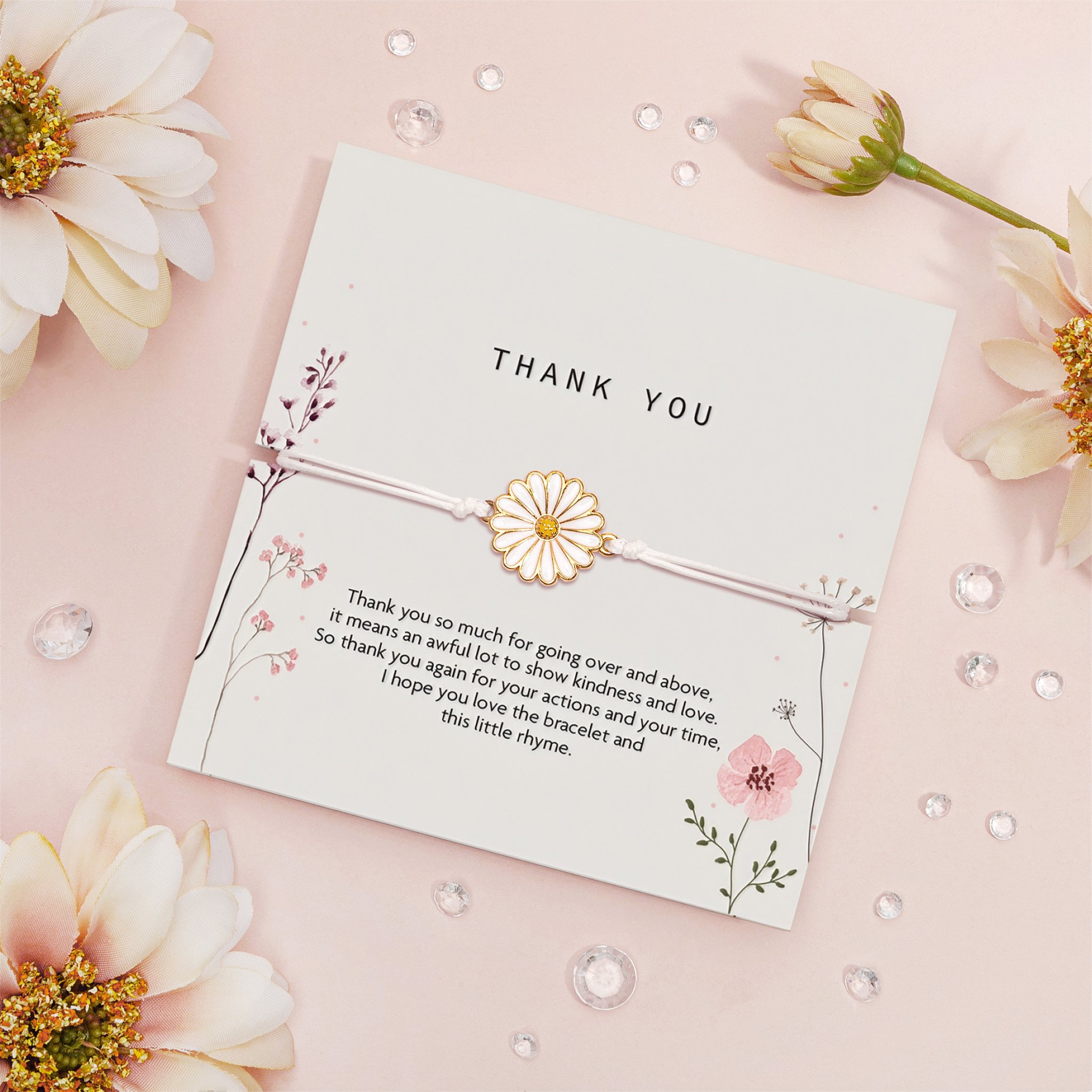 Thank-You-Karte mit Gänseblümchen-Armband schräg auf Rosa, umgeben von Blüten und Glassteinen