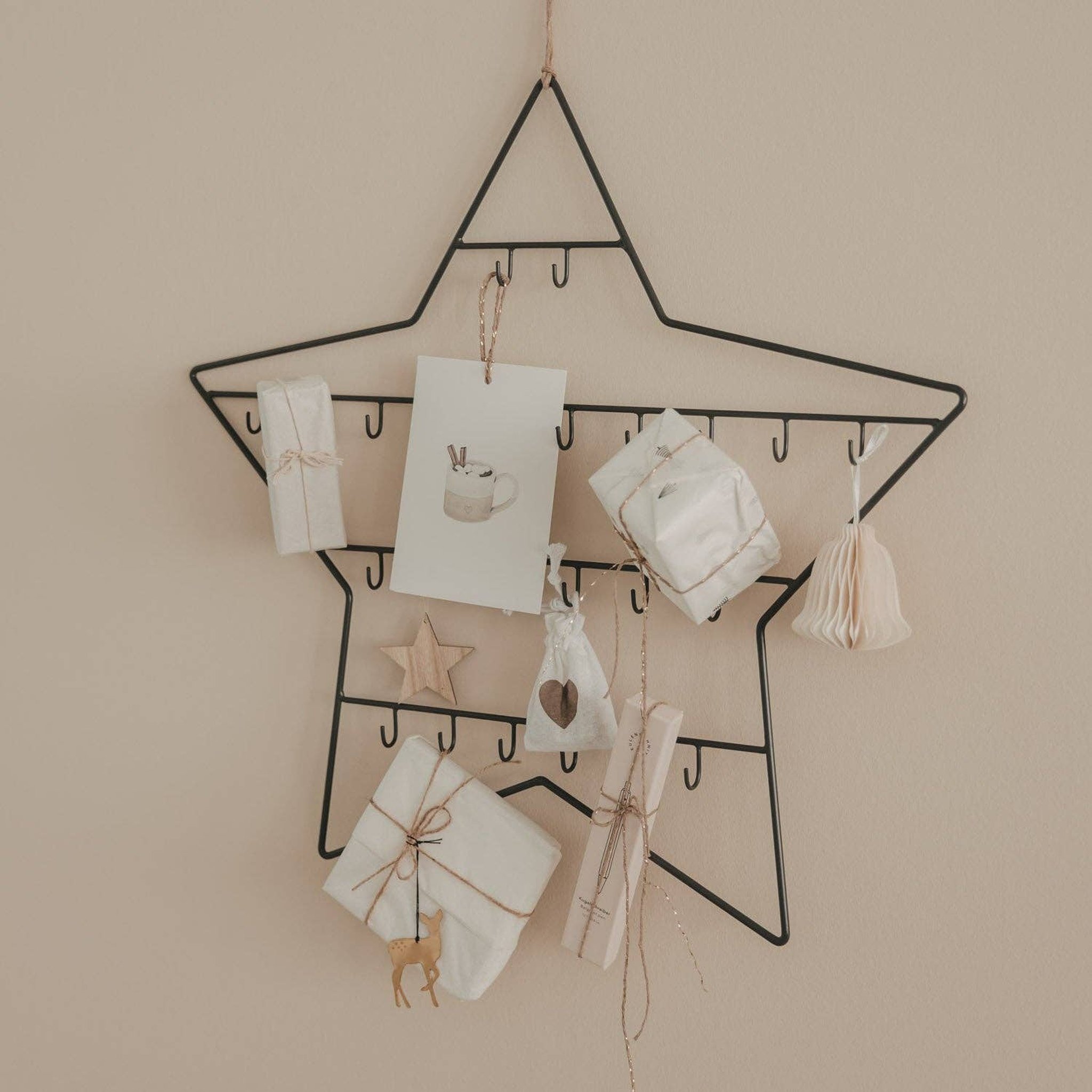Metal star advent calendar on a beige wall with wooden stars and paper ornaments